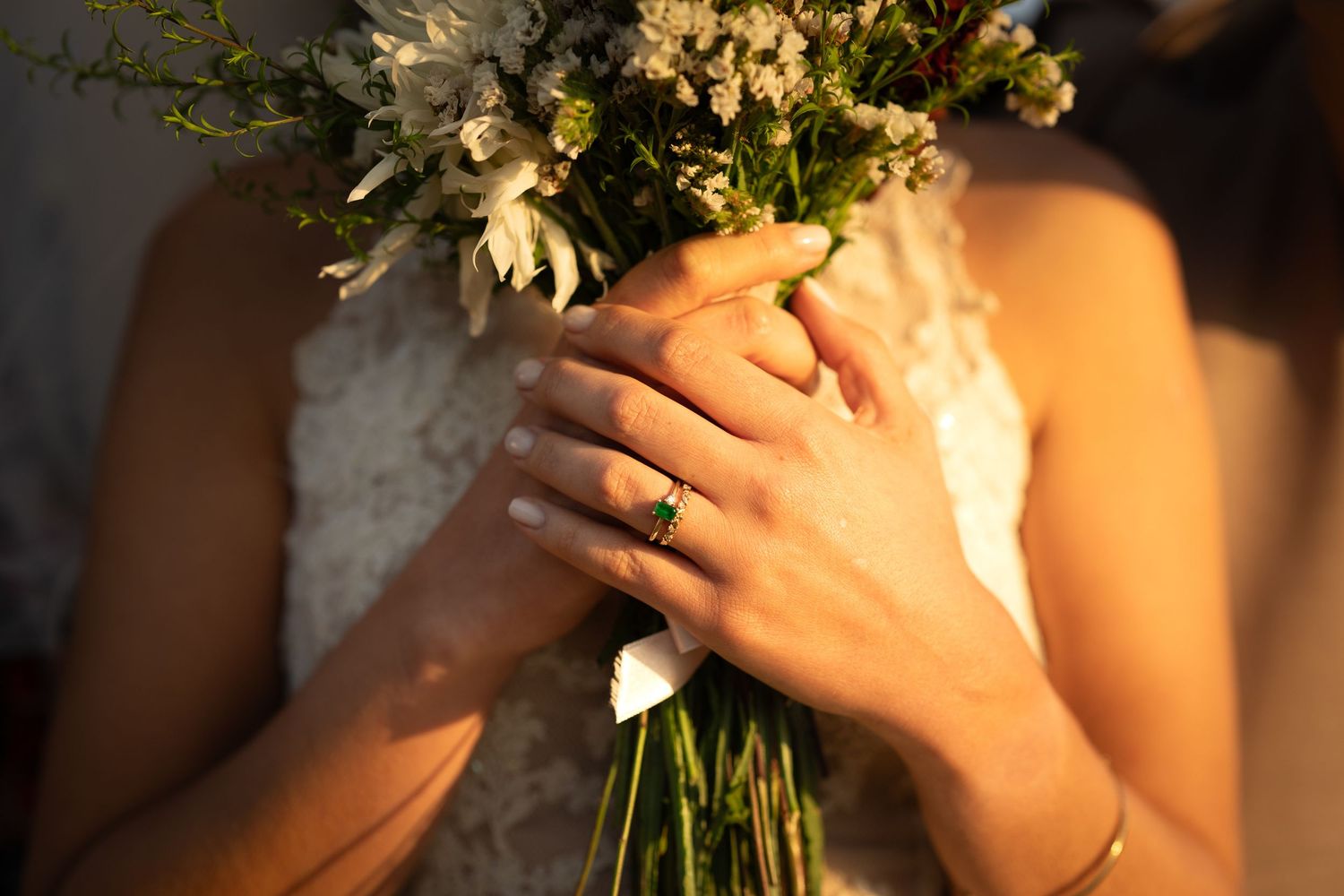 Bride holding a white and green floral wedding bouquet in a lace dress.