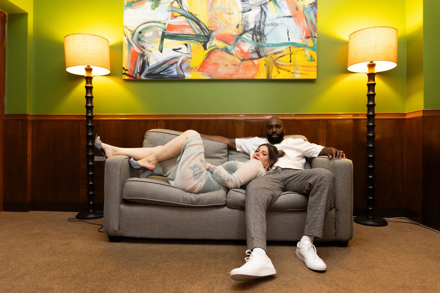 Couple relaxing on a gray sofa beneath a colorful abstract painting in a stylish room.