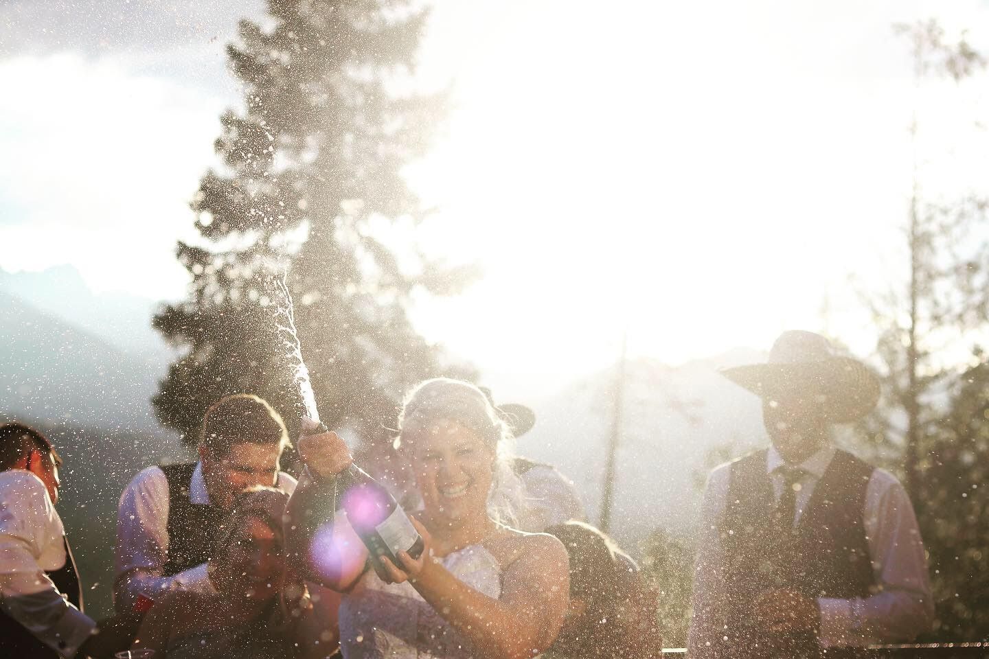 Bride and groom celebrating outdoors with sunlight and mountain trees in background.
