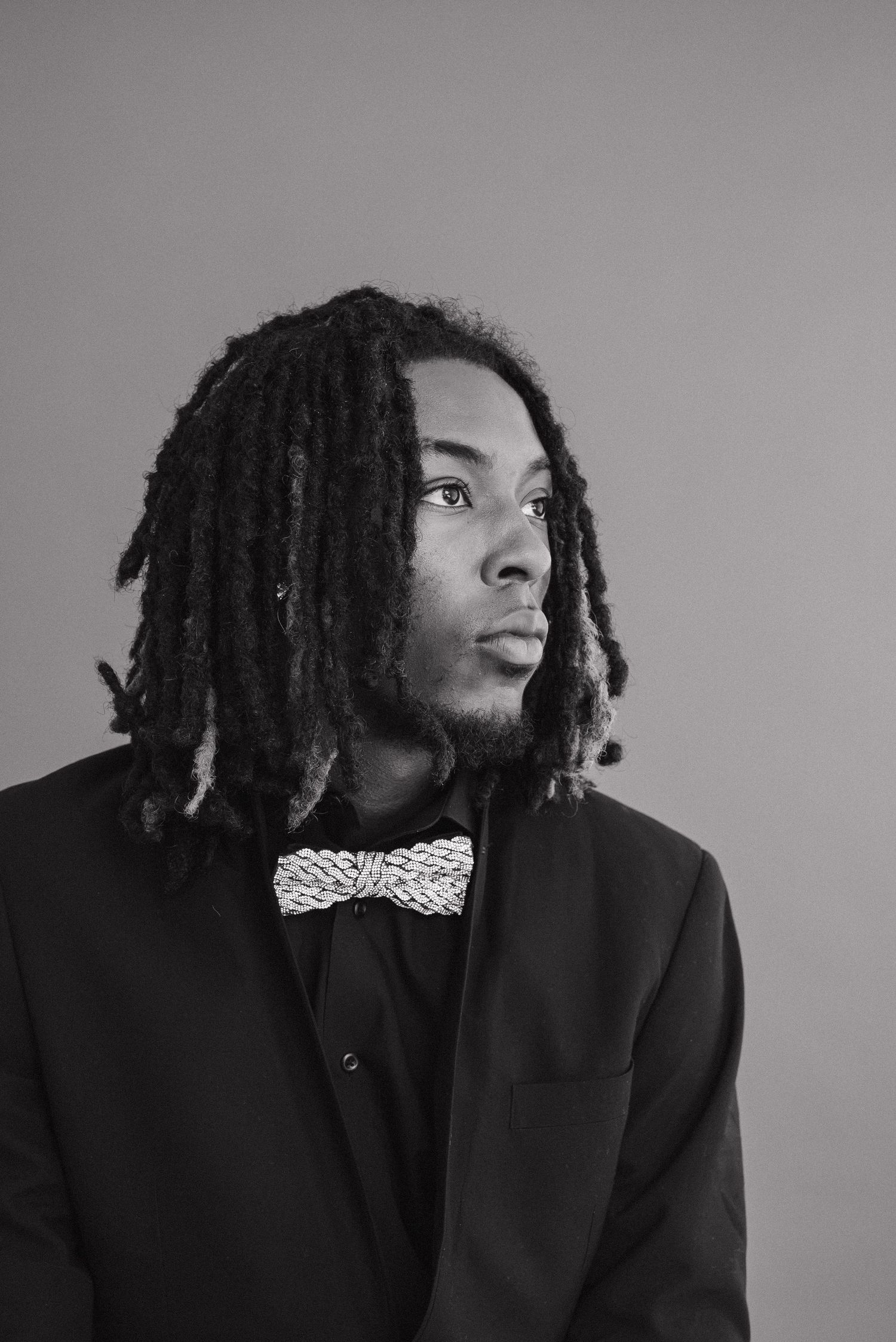 Black and white portrait of a young man with dreadlocks wearing a bow tie and suit jacket.