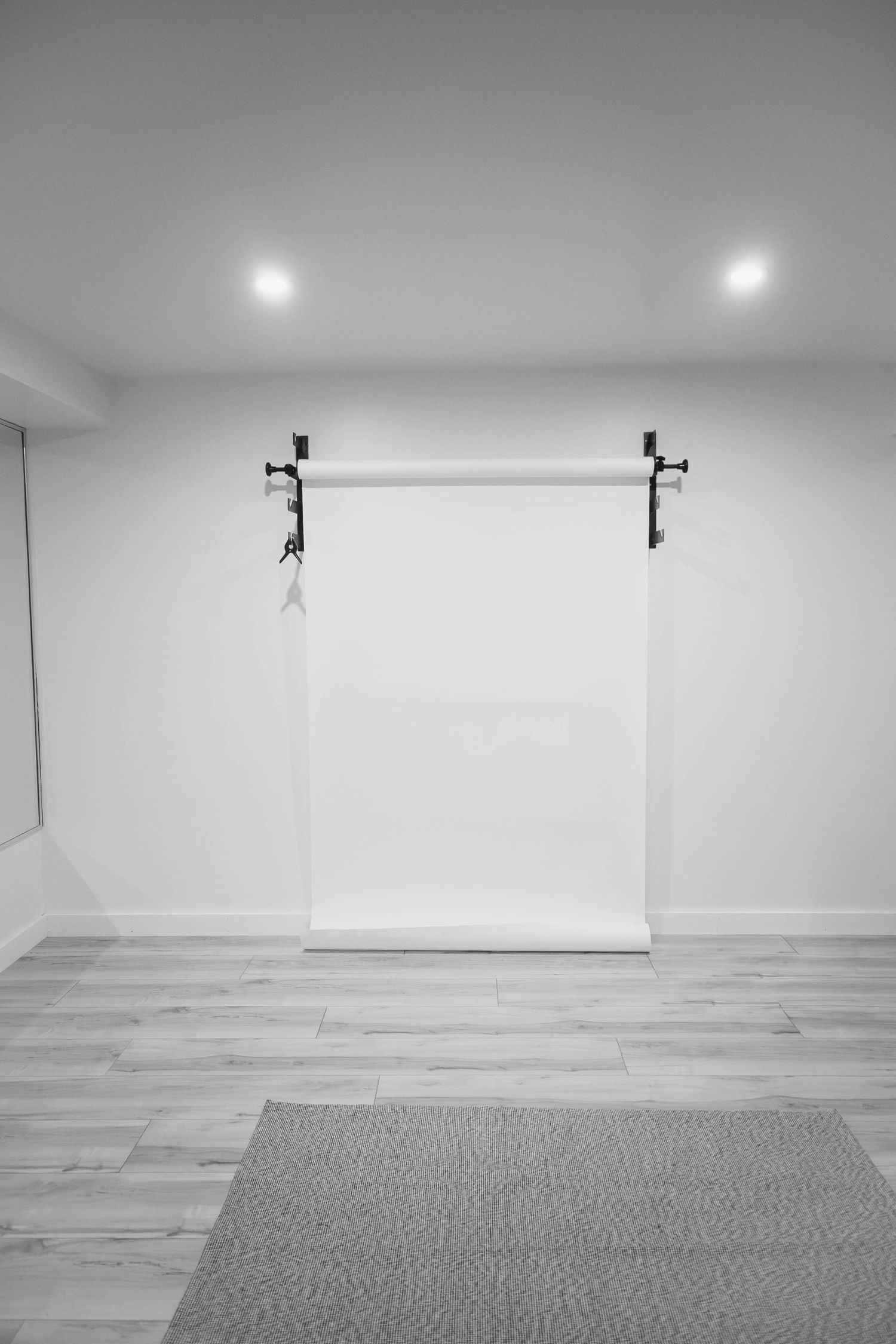 Minimalist photography studio with white backdrop on wall-mounted roller, hardwood floors, and recessed lighting.
