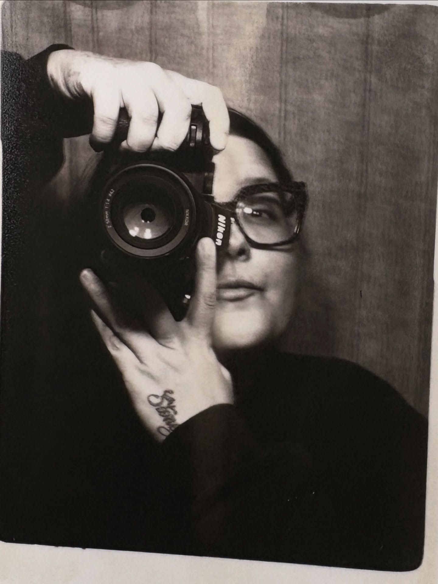 Person taking a black and white mirror selfie with a Nikon camera wearing glasses.