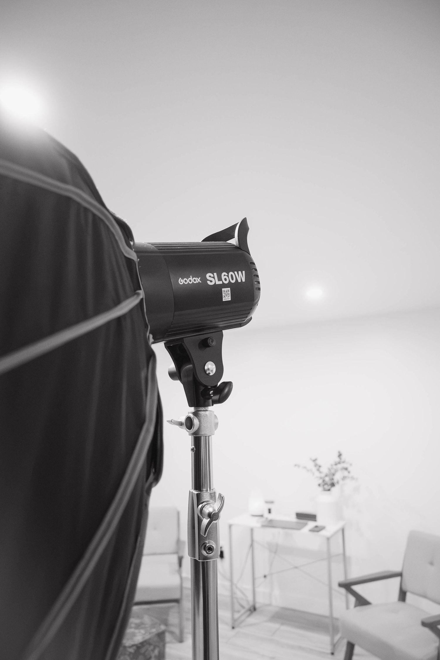 Black and white photo of a Godox SL60W studio light on a stand with a softbox modifier in a photography studio.