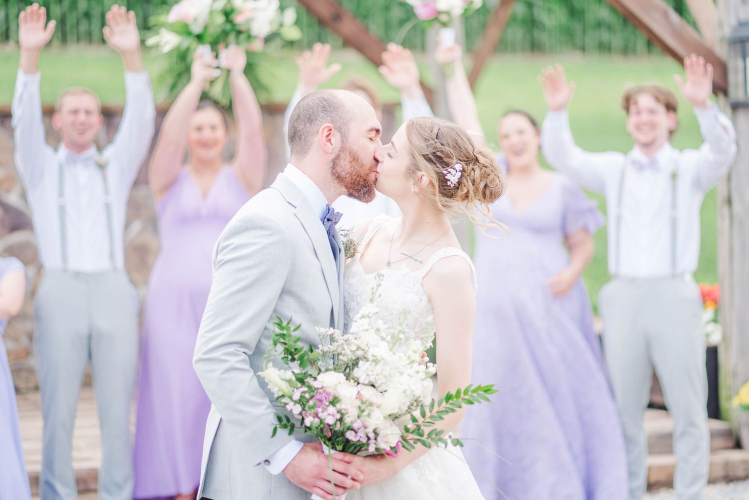 Bride and groom kissing with bridal party cheering behind them at Joiner Farms in Northern Cambria, Pennsylvania