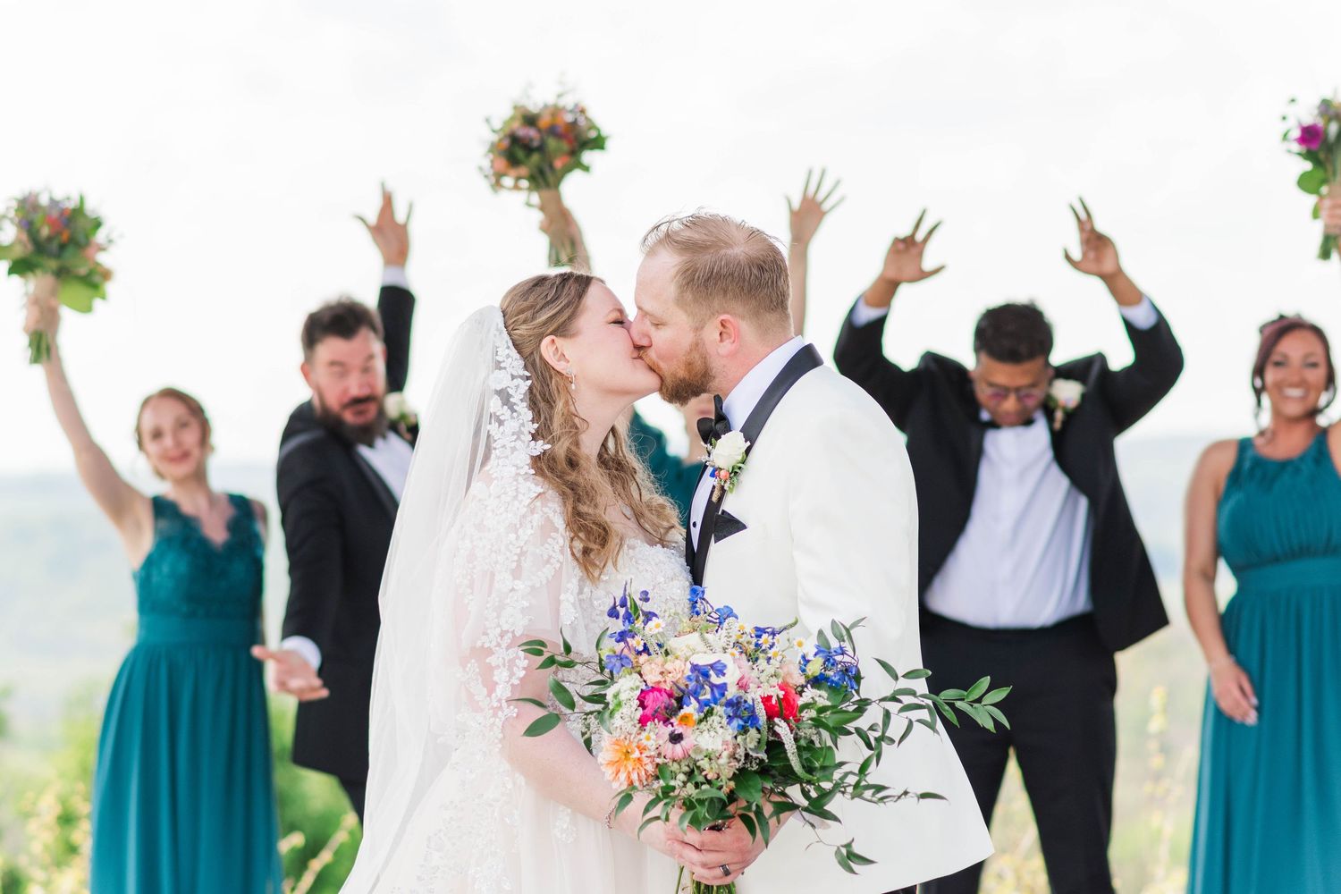 Bride and groom kissing with bridal party celebrating behind them at the Roost in Mahaffey, Pennsylvania