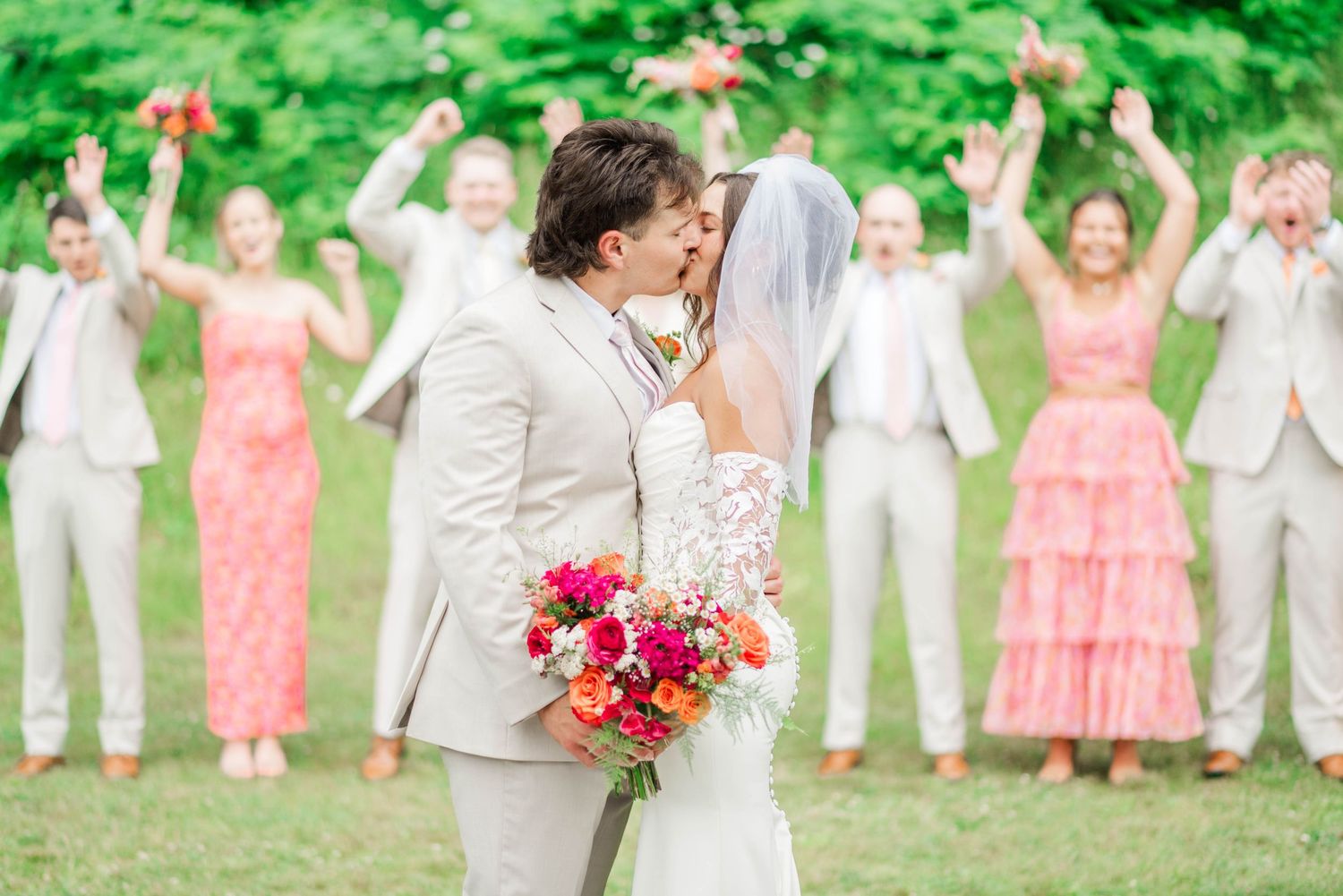 Bride and groom kissing with bridal party cheering behind them at Whispering Hollow Estates in Pleasantville, Pennsylvania