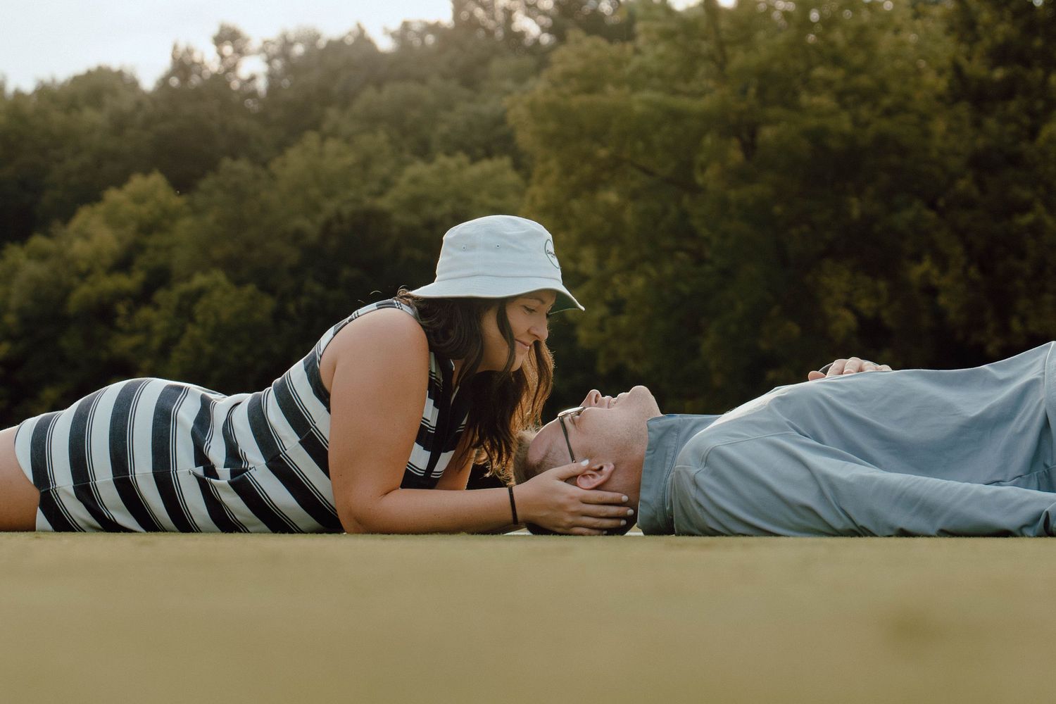 A romantic couple lying on a surface outdoors, the woman leaning down toward the man lovingly.