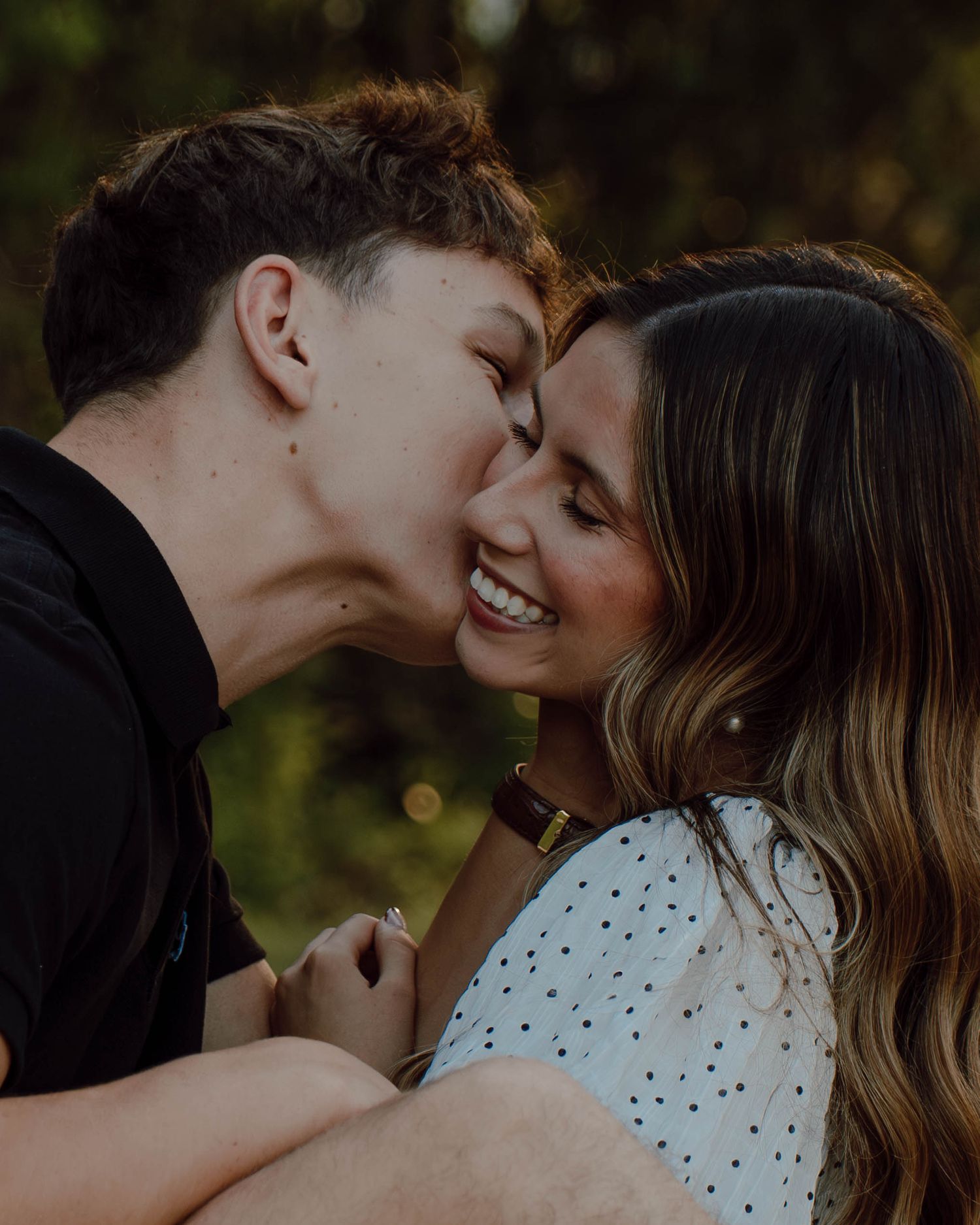 A young couple sharing a tender moment outdoors, as the man kisses the smiling woman on the cheek.