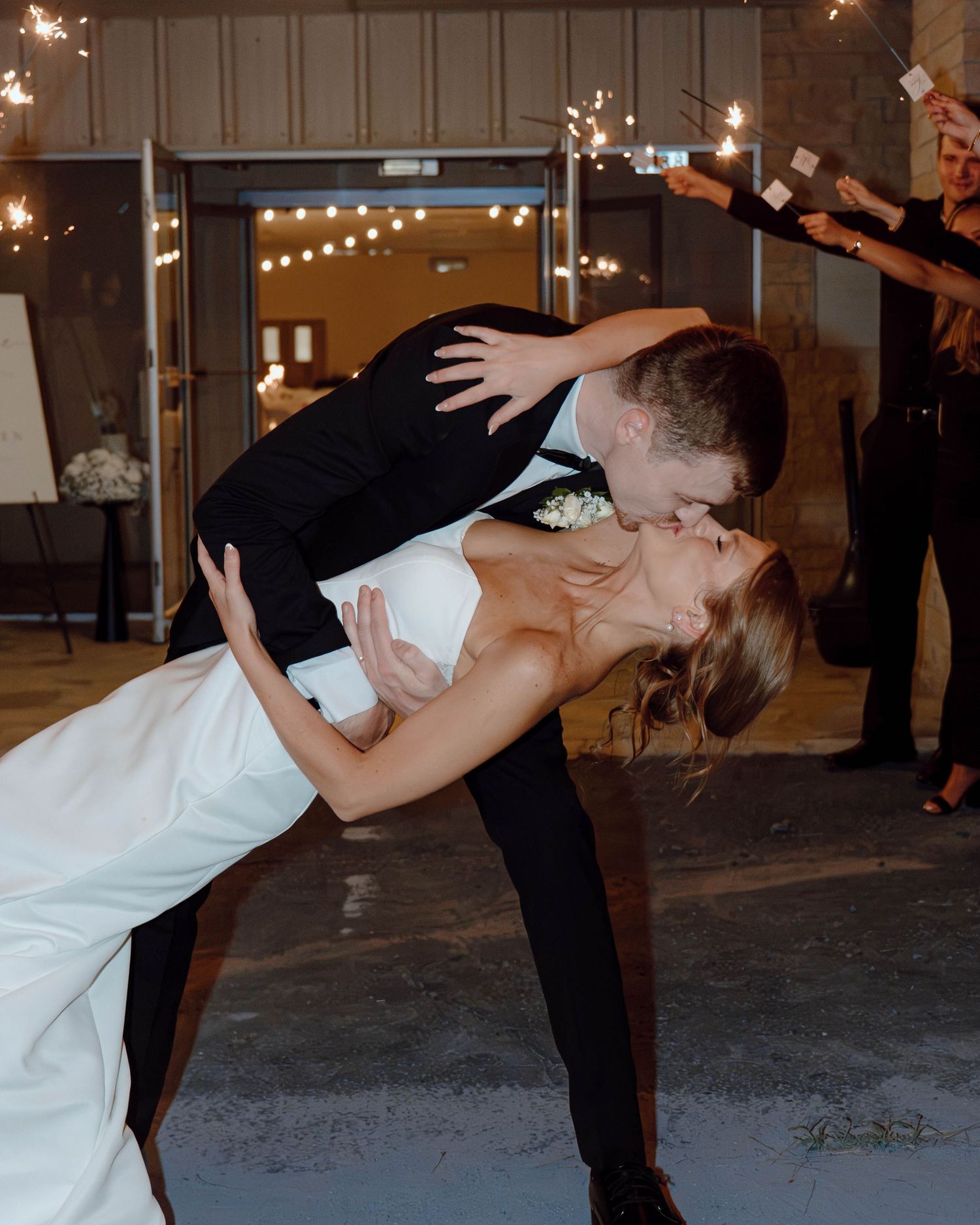 Bride and groom share a romantic dip kiss on the dance floor surrounded by sparklers at their wedding reception.