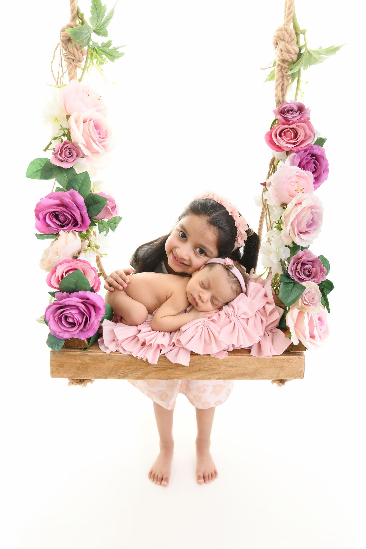 Older sister holding a sleeping newborn on a floral swing