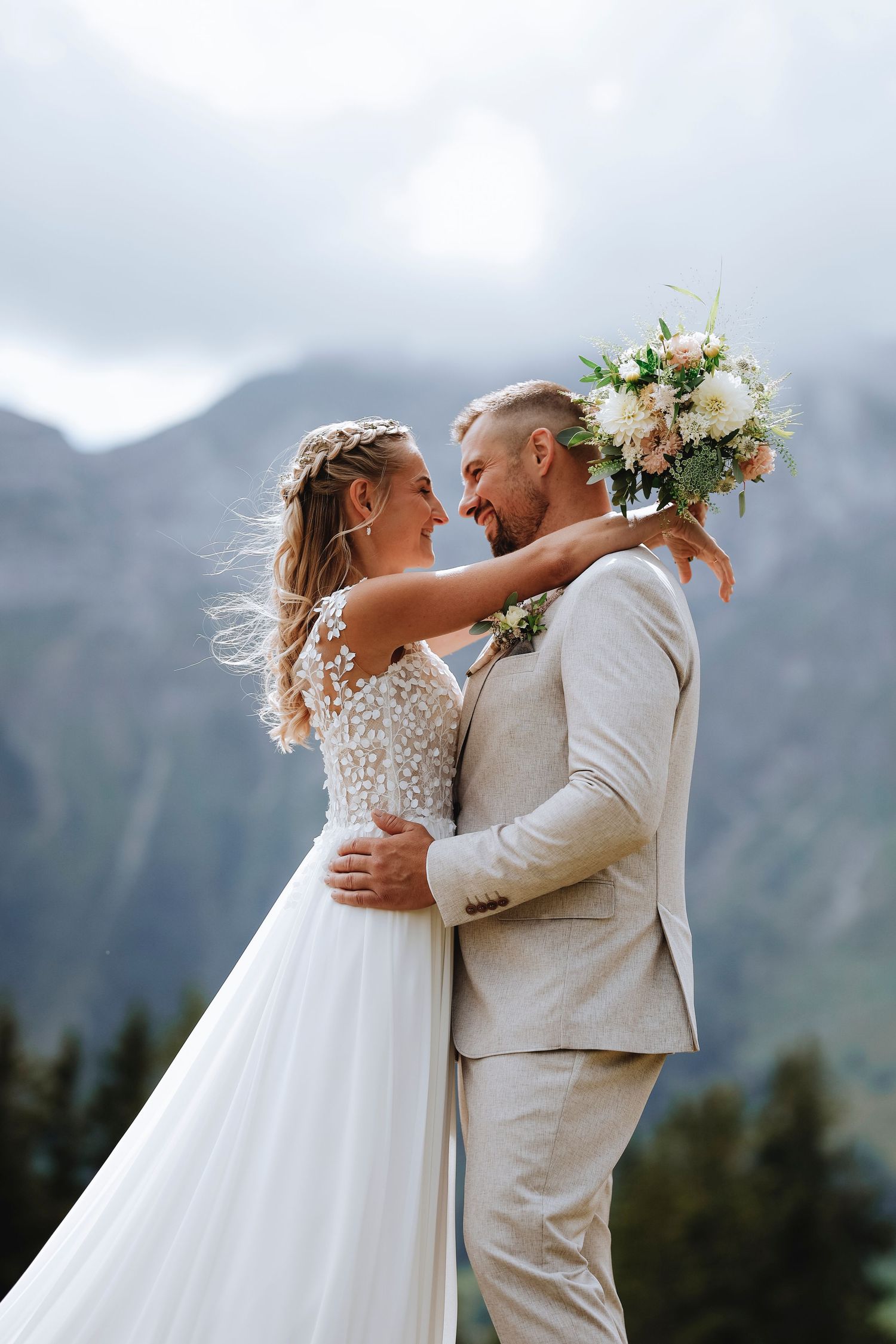 A bride and groom embrace and smile at each other with a stunning mountain backdrop on their wedding day.