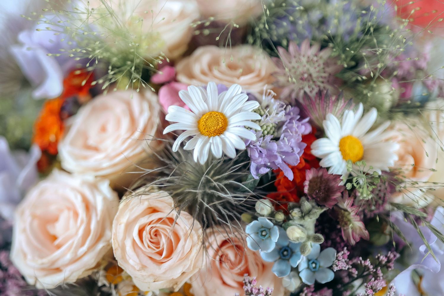 A beautiful wedding bouquet featuring peach roses, white daisies, and colorful wildflowers up close.