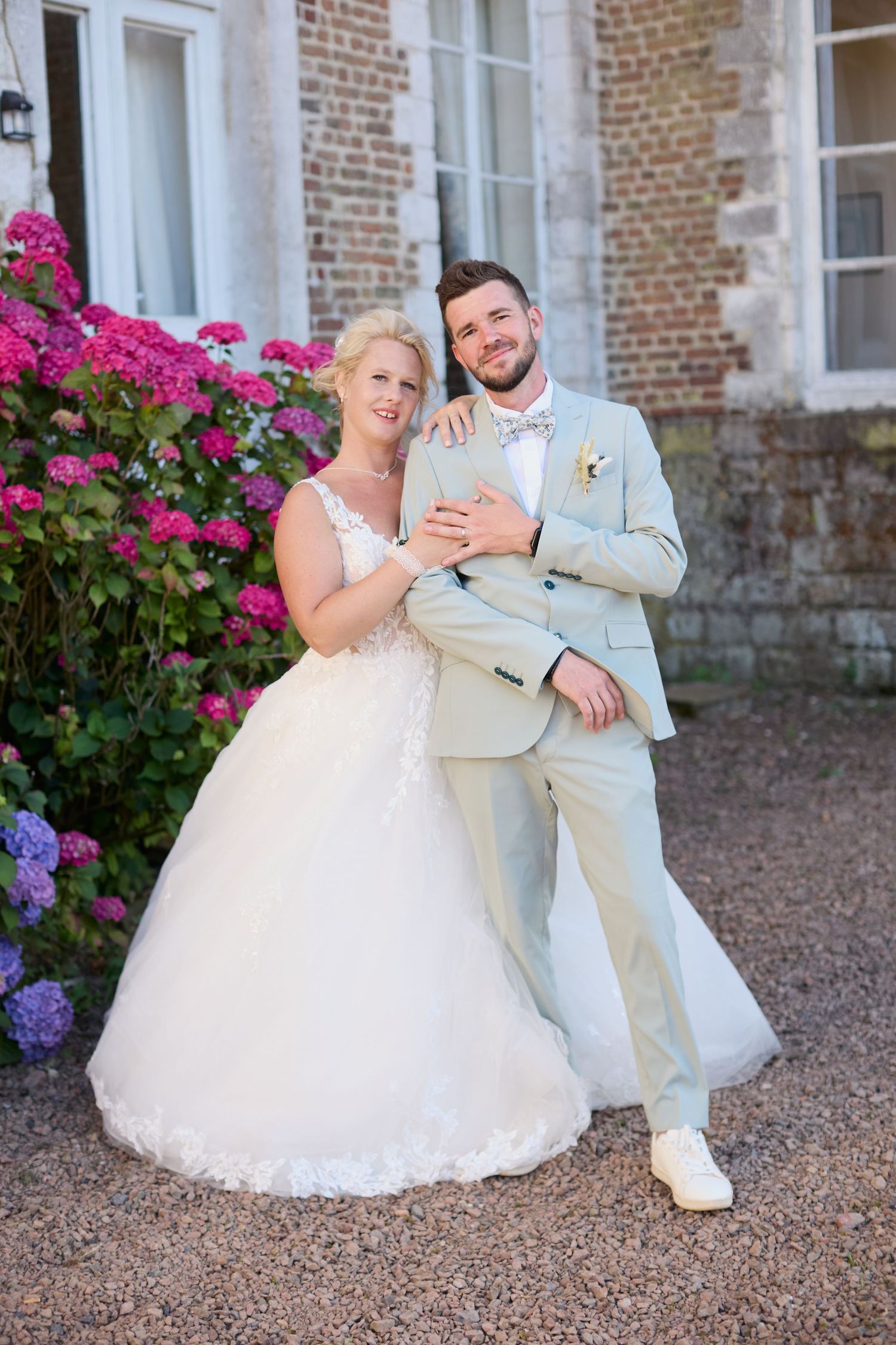 Portrait des mariés enlacés en extérieur devant la façade d'un château en briques