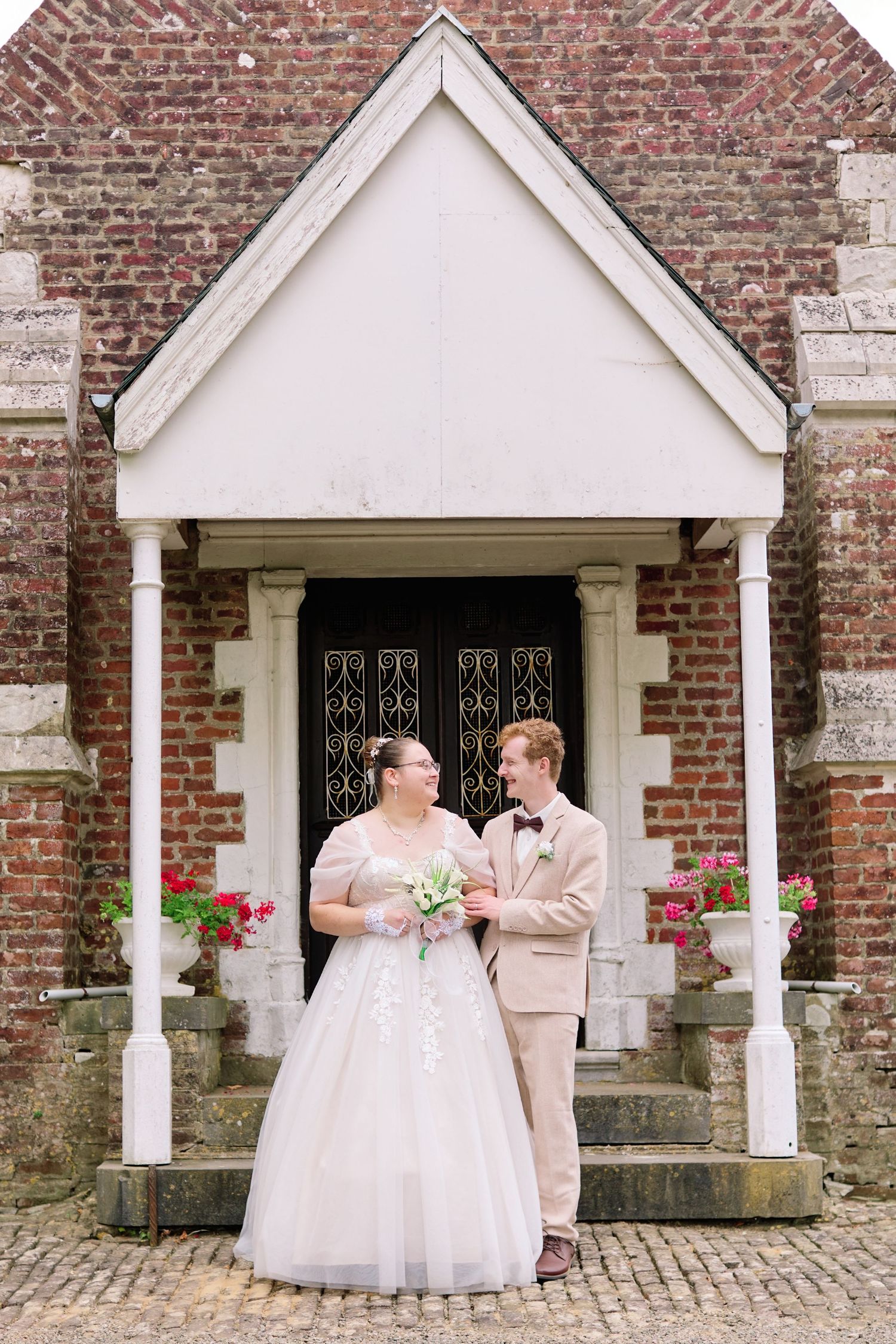 Portrait des mariés devant l’entrée d’une église en briques