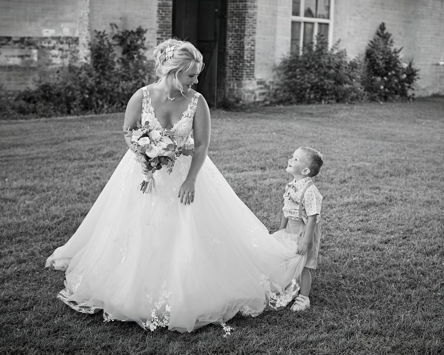 Mariée marchant dans un jardin avec un jeune enfant en noir et blanc
