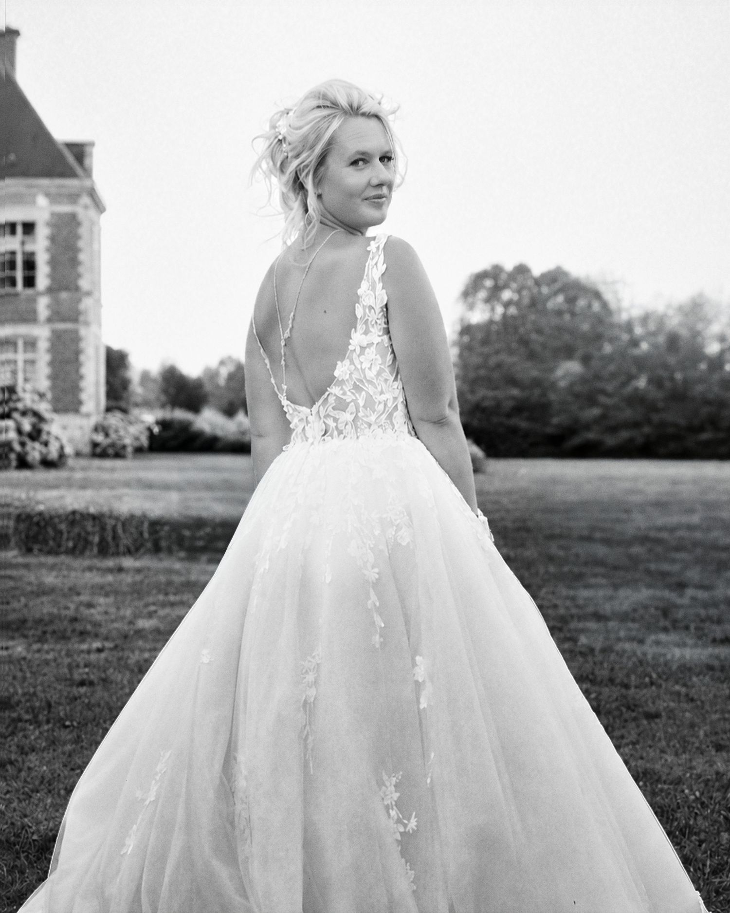 Portrait de dos de la mariée en noir et blanc devant le domaine de réception