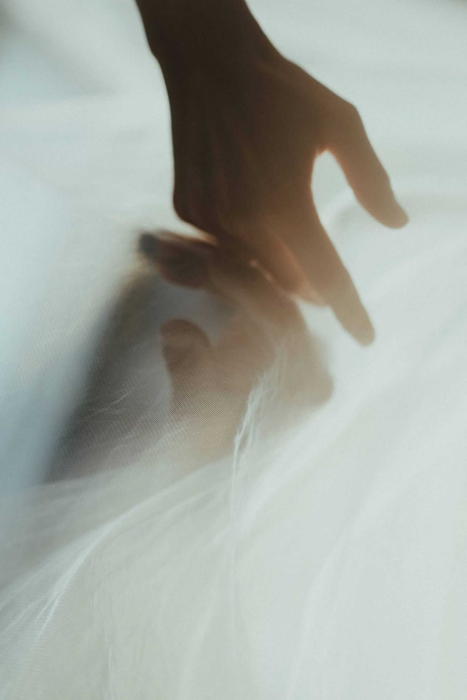 A hand reaching toward a white feather on a soft surface, bathed in warm backlight.