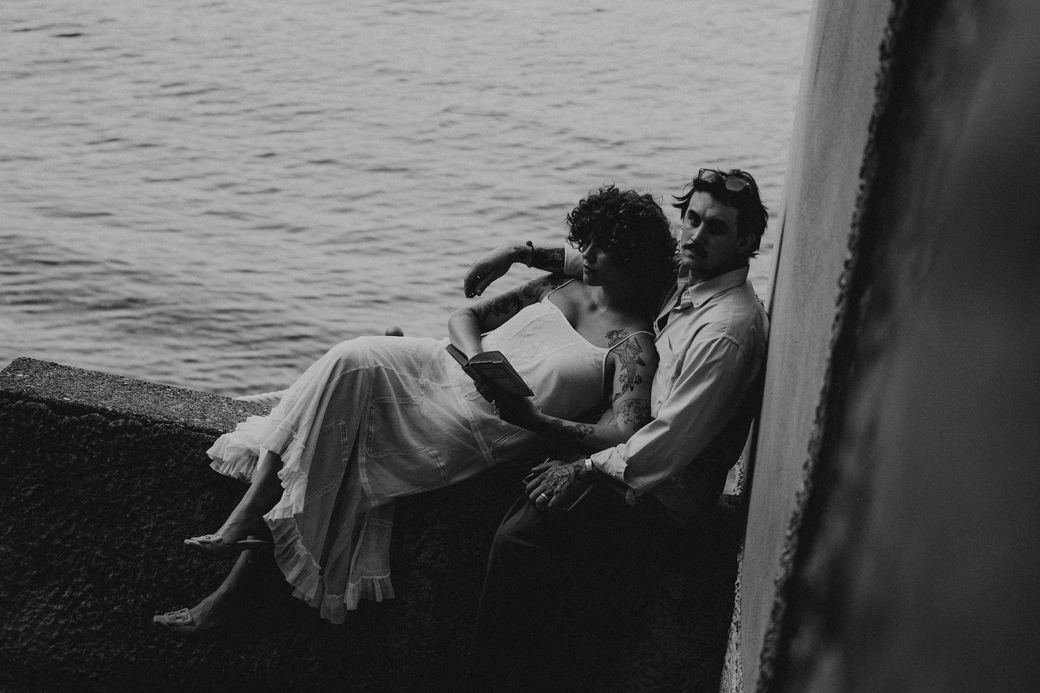 Black and white photo of couple relaxing together on stone steps beside the sea.