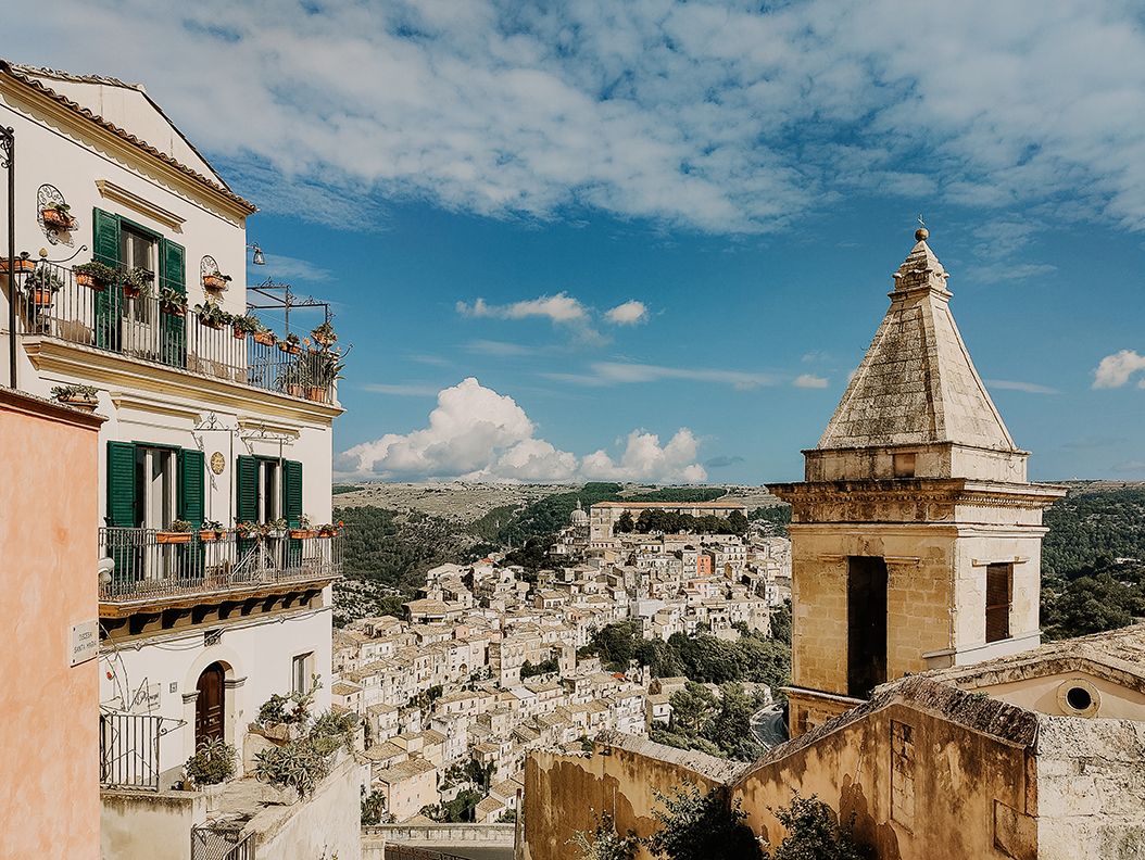 Panoramic view of ancient Ragusa Ibla, Sicily, with baroque architecture and vast cityscape under blue sky.