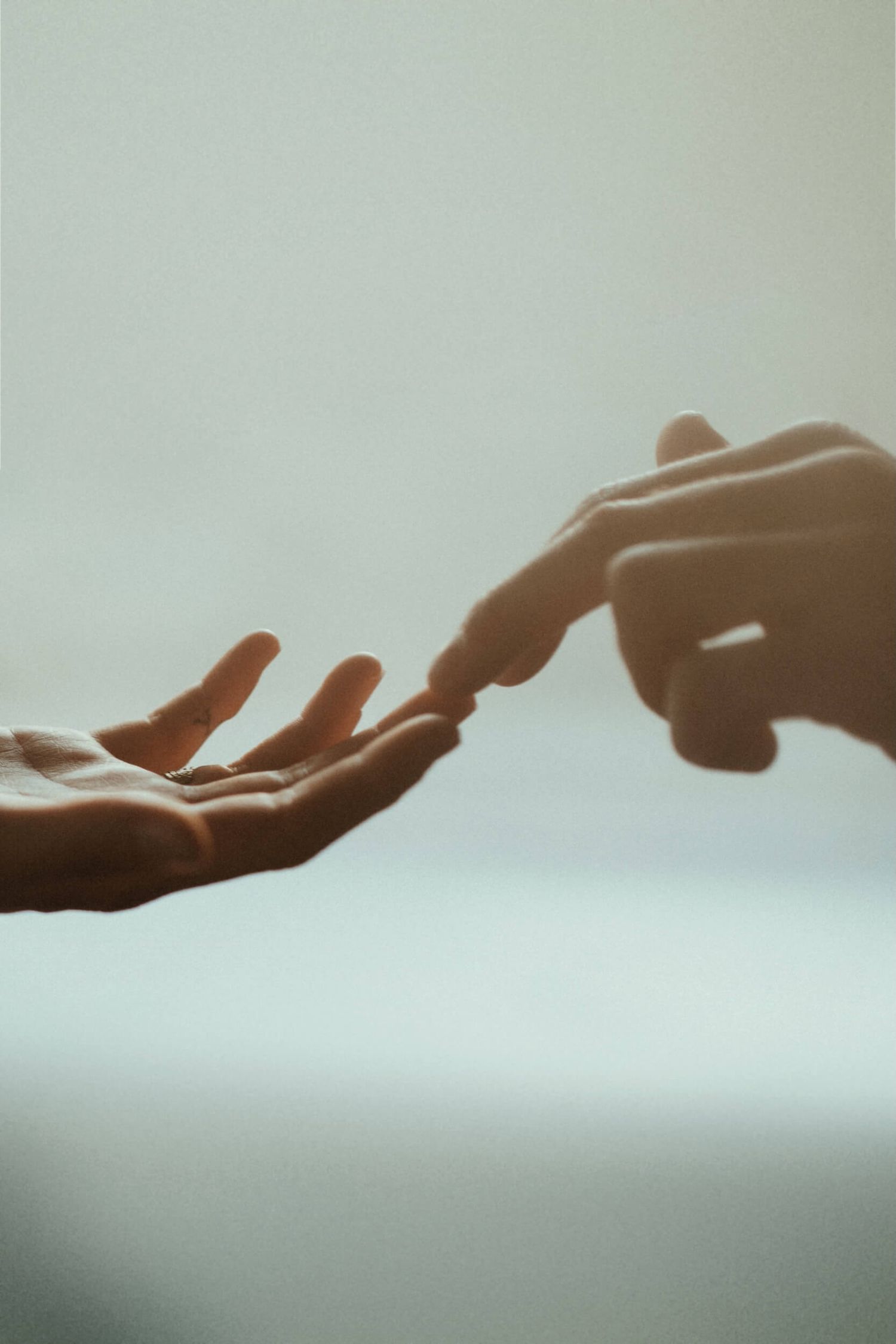 Two hands reaching toward each other with fingertips touching against a soft white background.
