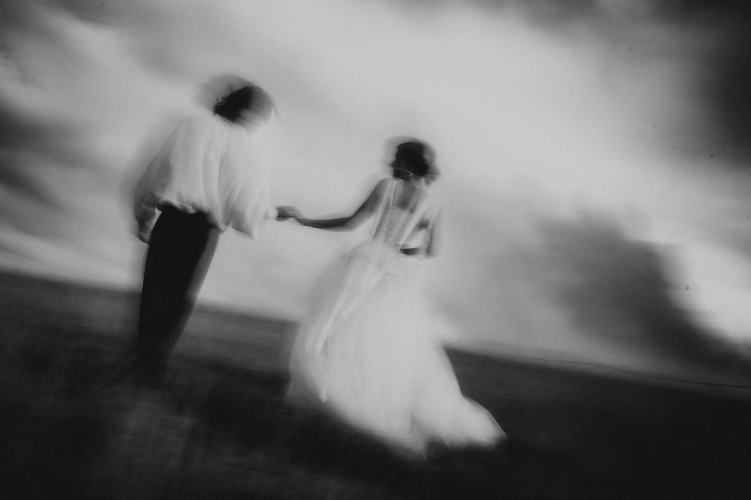 Black and white blurred motion shot of couple dancing in wedding attire outdoors.