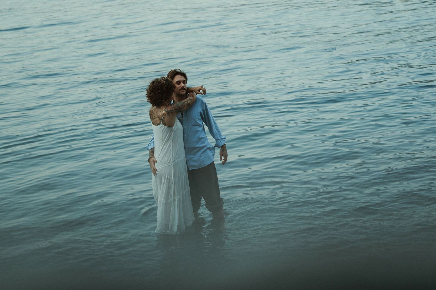 Couple embracing while standing in the calm sea water at dusk.