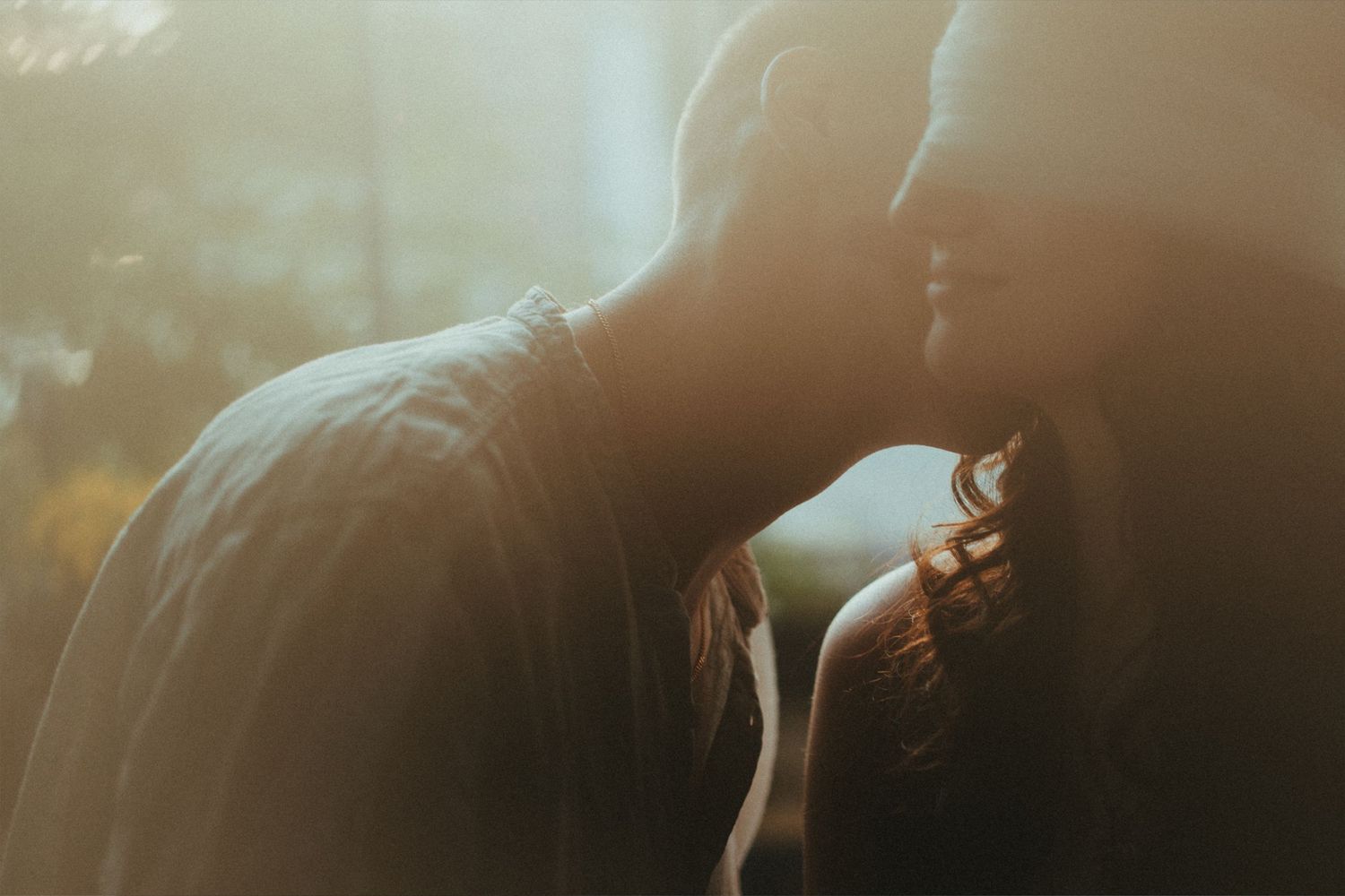 Romantic couple sharing an intimate moment in warm golden sunlight, silhouetted against a soft bokeh background.