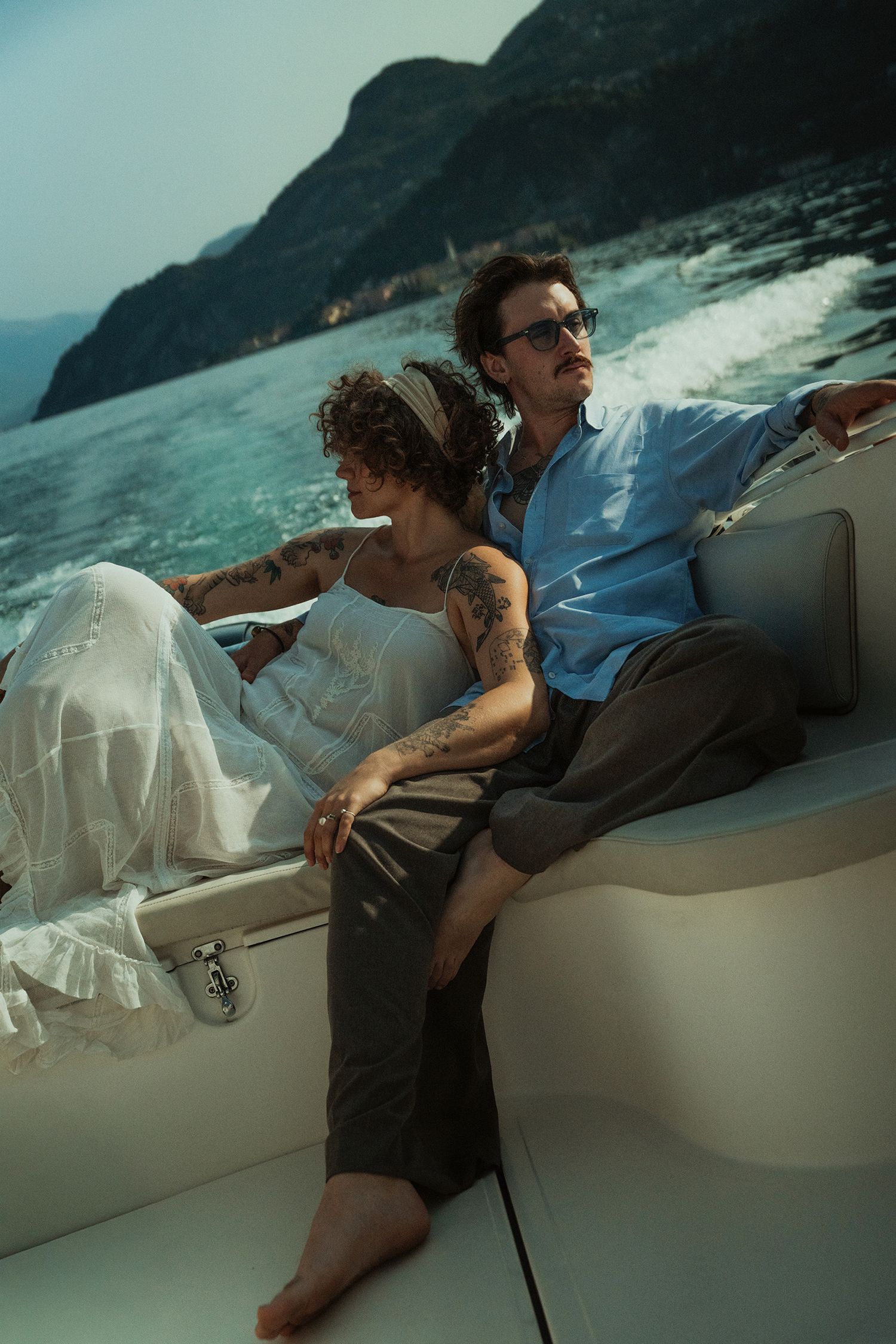 Couple relaxing on a speedboat with mountain and lake scenery in the background.