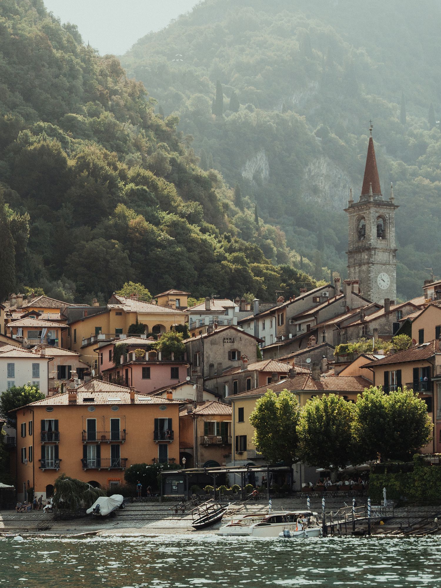 Picturesque Italian lakeside village with colorful buildings, church tower and lush green mountains.