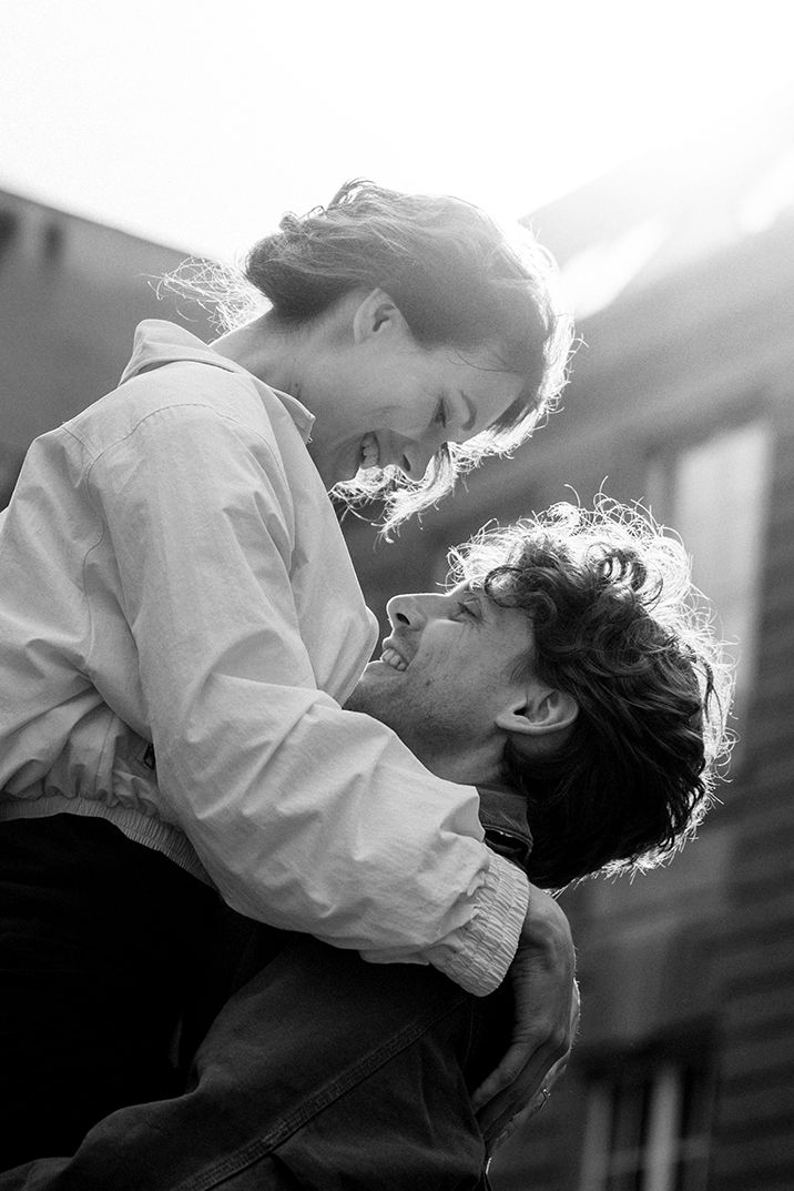 Black and white photo of a joyful couple embracing outdoors, woman lifted as they share a loving smile.