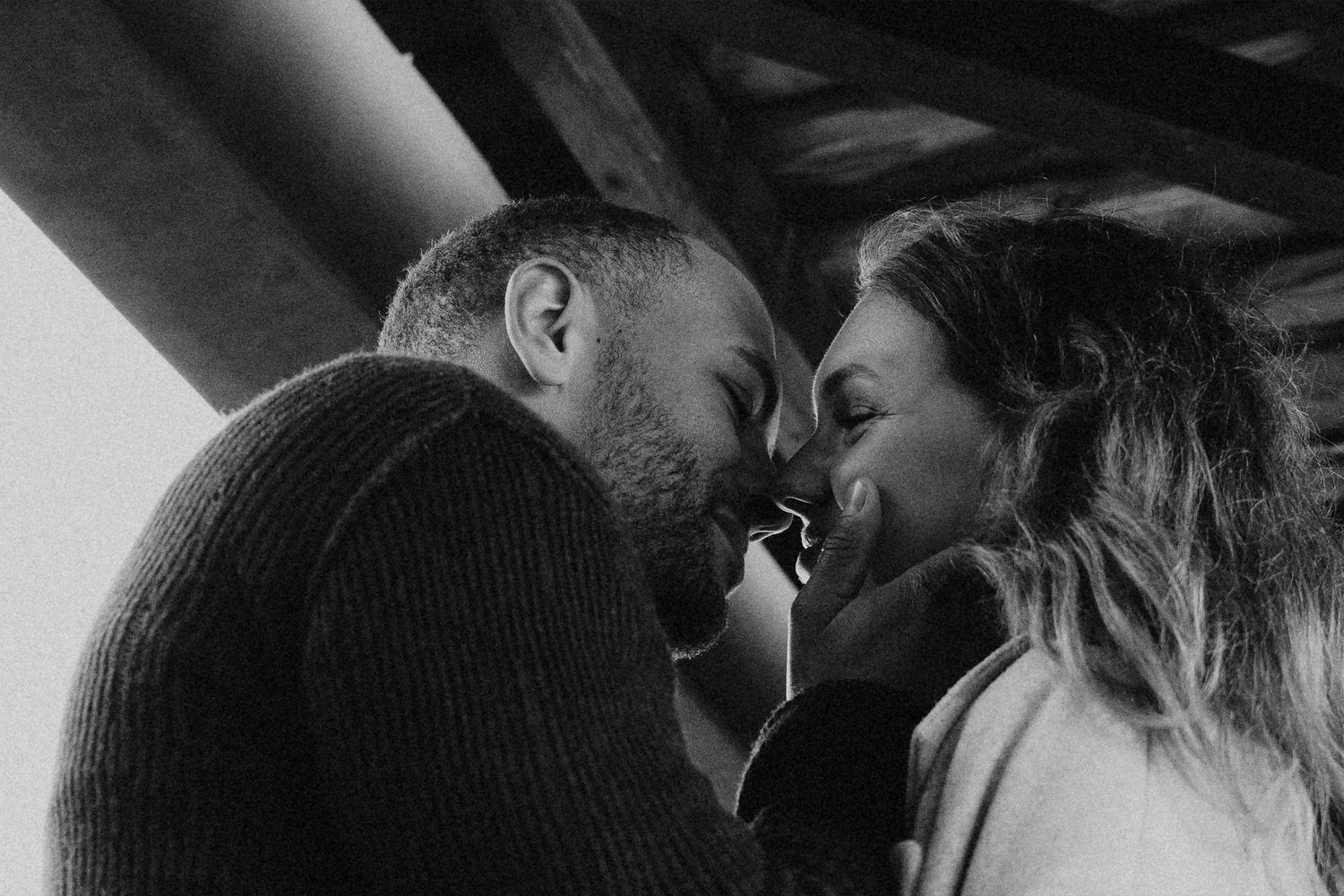 Black and white photo of a romantic couple sharing an intimate moment, foreheads touching tenderly indoors.