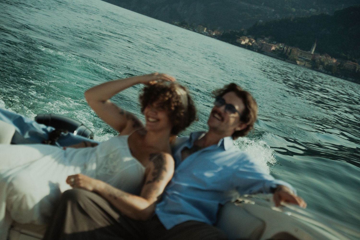 Happy couple relaxing on a speedboat on a mountain lake, woman in a white dress, the man in a blue shirt wearing sunglasses.