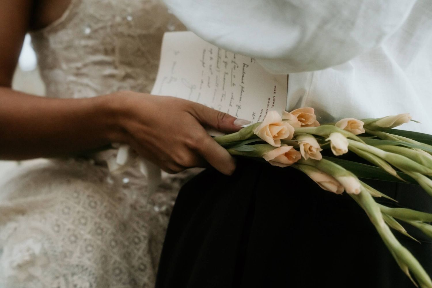 Close-up of a bride holding flowers and a handwritten letter in a lace wedding dress.