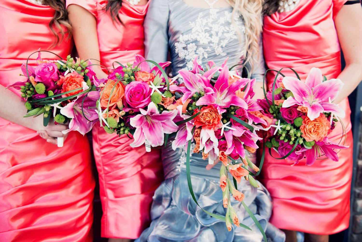 Bridesmaids in coral dresses holding colourful bouquets of lilies and roses during a wedding celebration.
