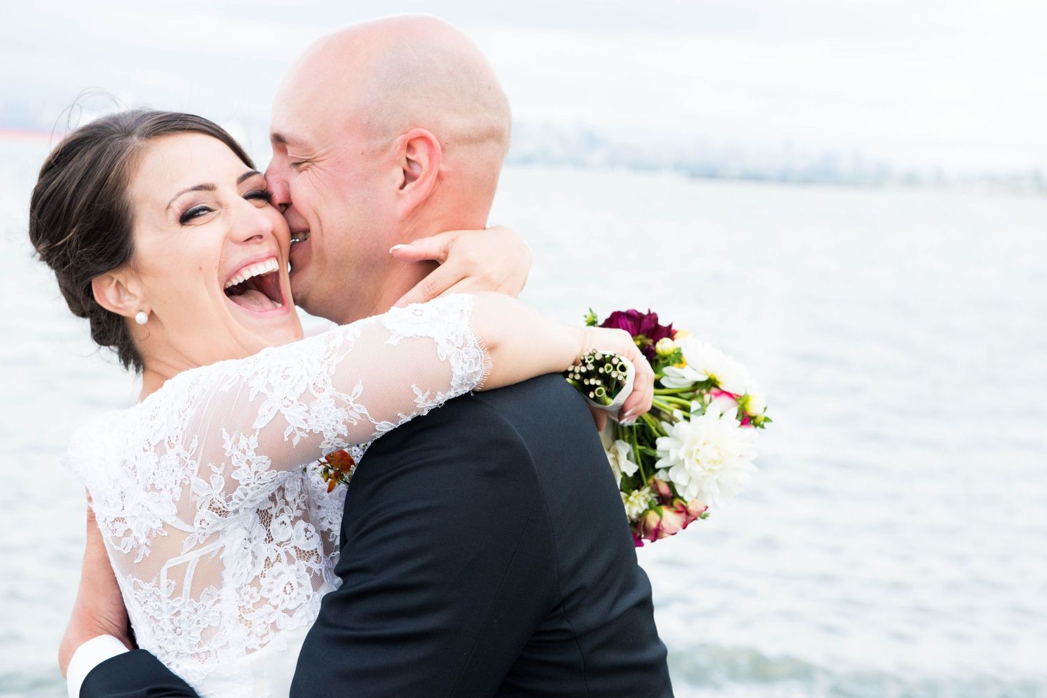 Bride laughing as the groom kisses her cheek during their wedding portraits at Spanish Banks in Vancouver, British Columbia.