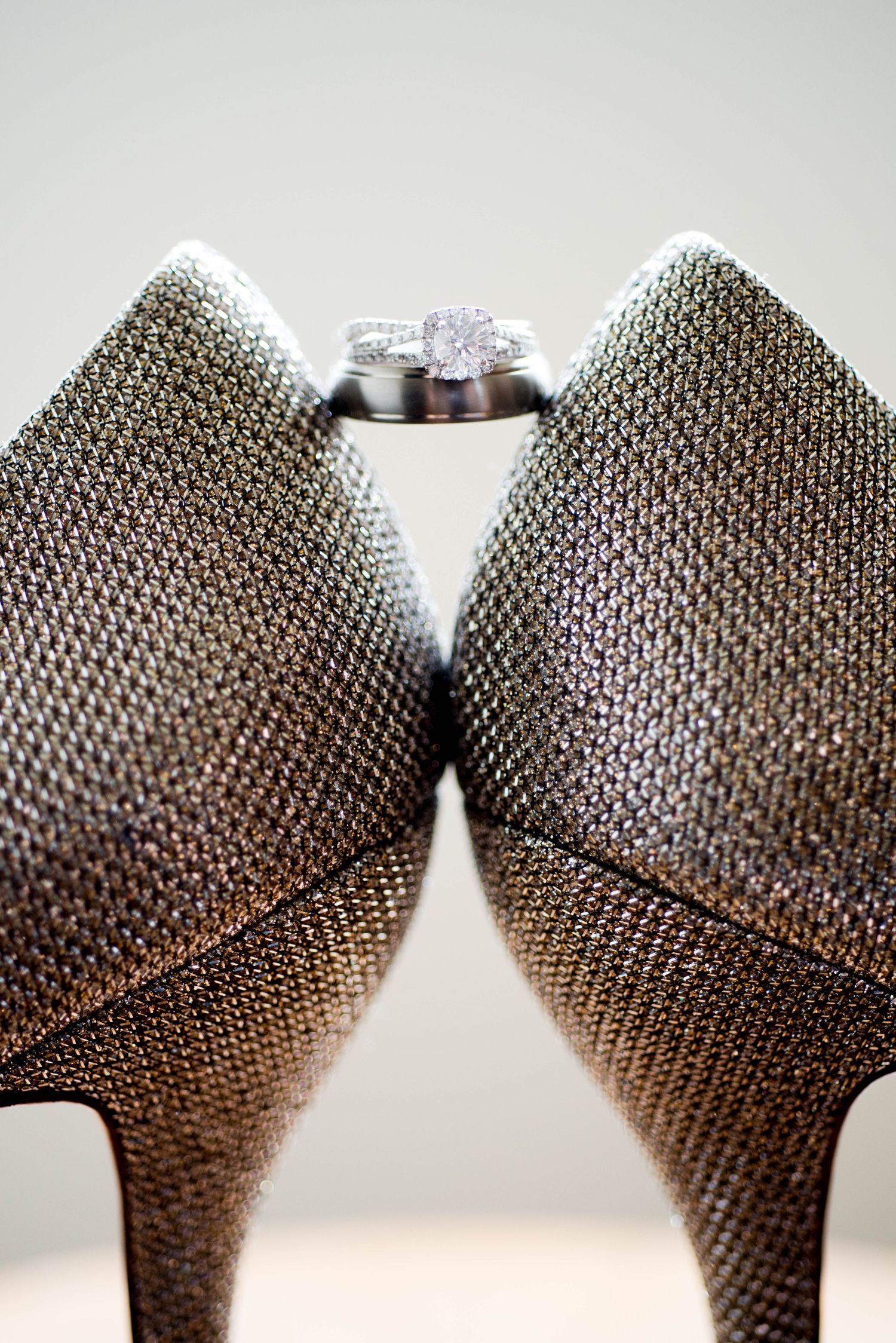 Diamond engagement ring displayed between two glittering silver high-heeled shoes.