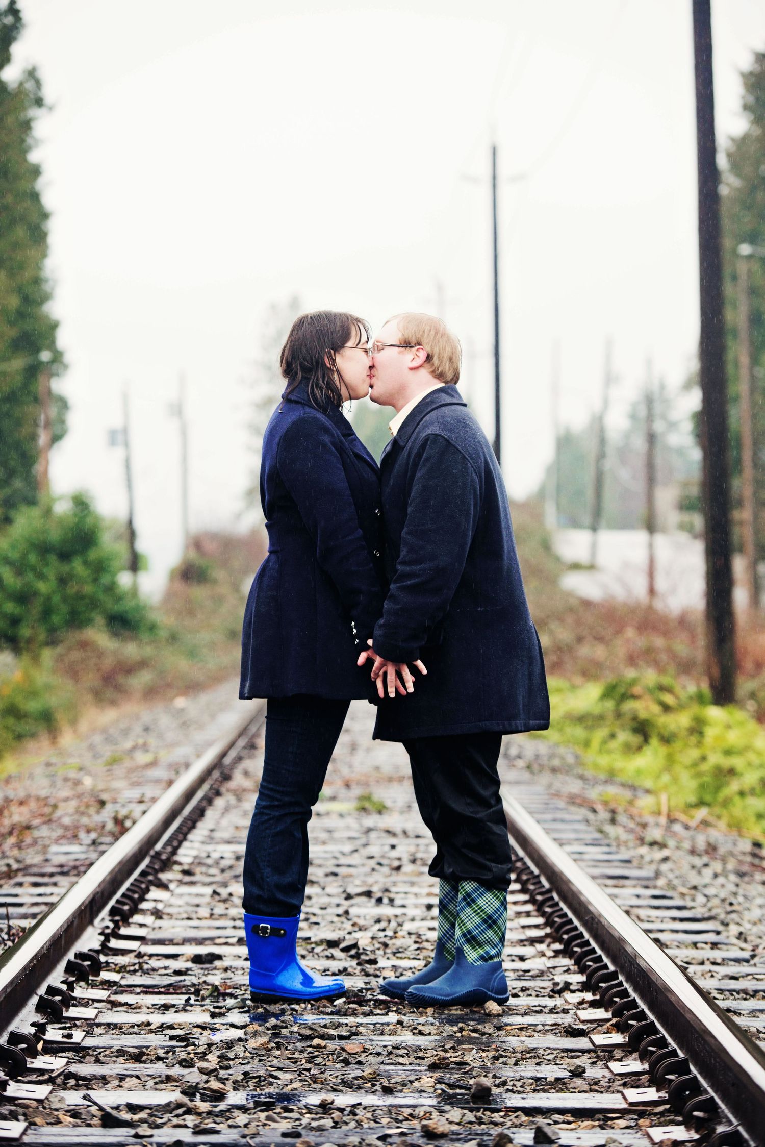 Couple kissing on rain-soaked railway tracks during an engagement session in White Rock, British Columbia.