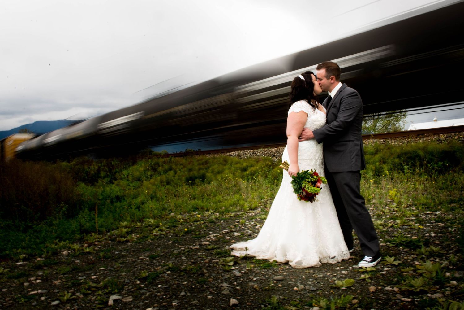 Bride and groom kissing beside railway tracks as a train passes in the background in Chilliwack, British Columbia.
