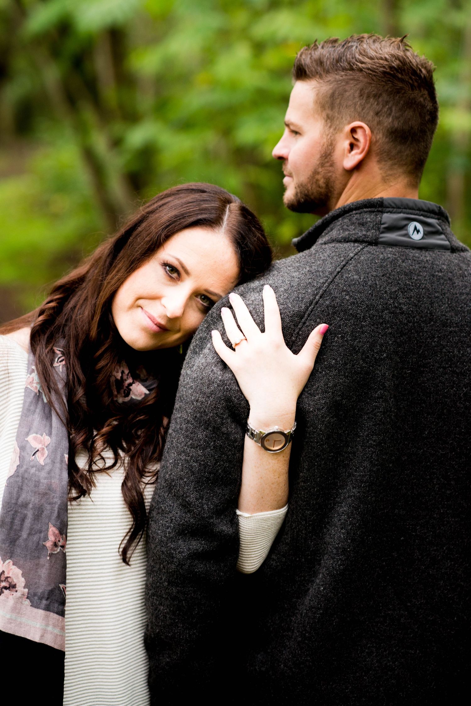 Woman resting her head on her partner's shoulder while showing her engagement ring during an engagement session.