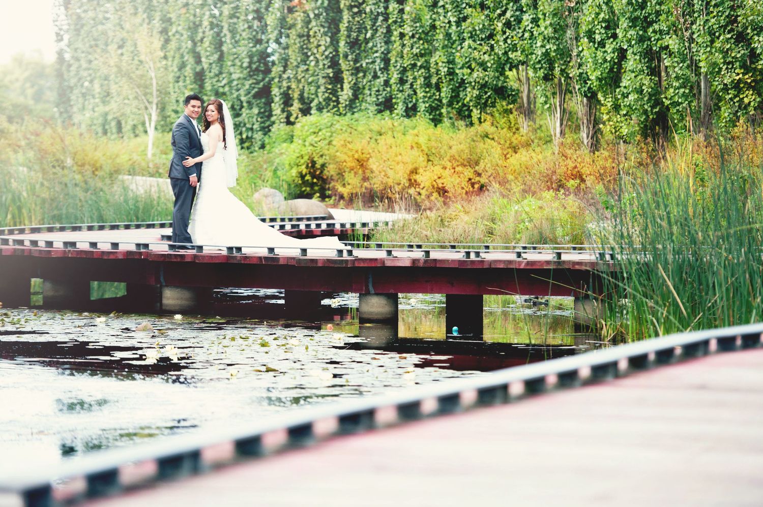 Bride and groom standing together on a dock surrounded by lush greenery during their wedding portraits.