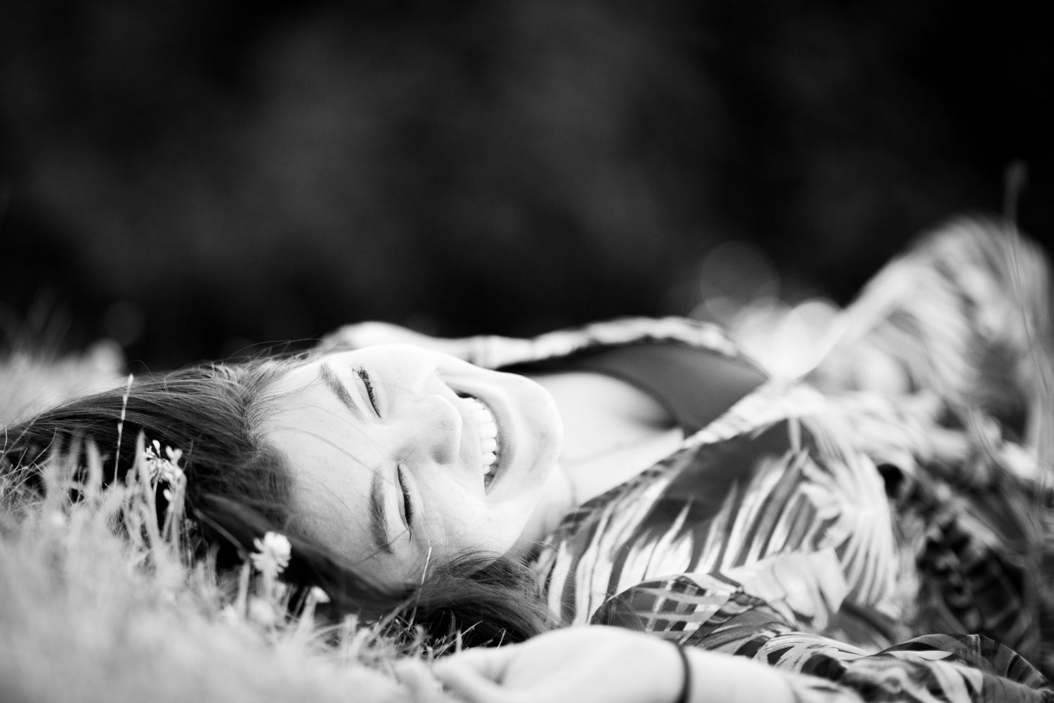 Black-and-white graduation portrait of a young woman laughing while lying in the grass in Chilliwack, British Columbia.
