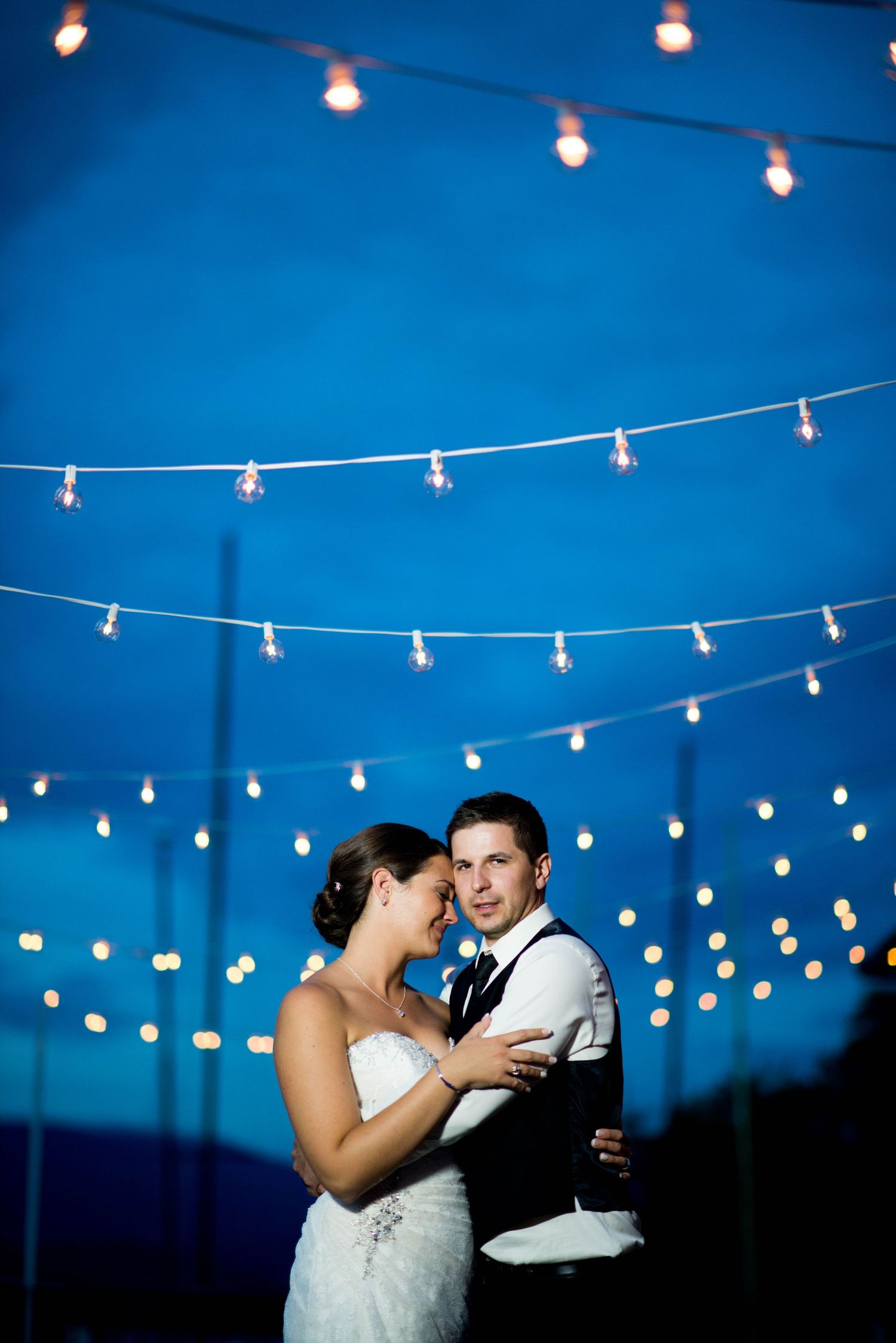 Bride and groom sharing their first dance beneath string lights at an evening wedding reception.
