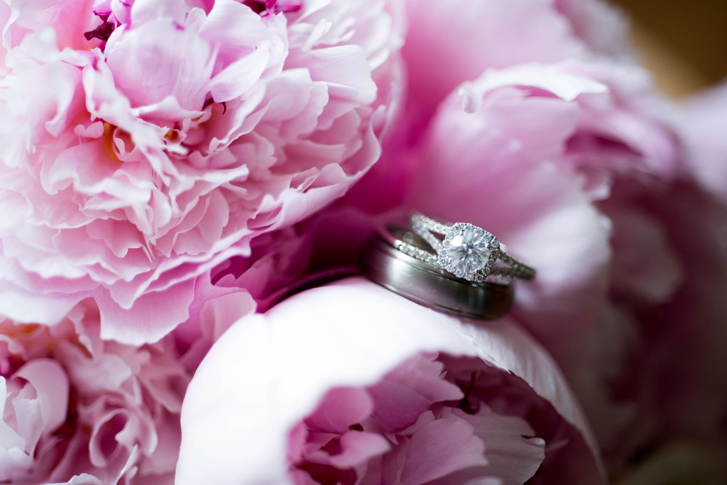 Diamond engagement ring and wedding band resting among soft pink peony flowers.