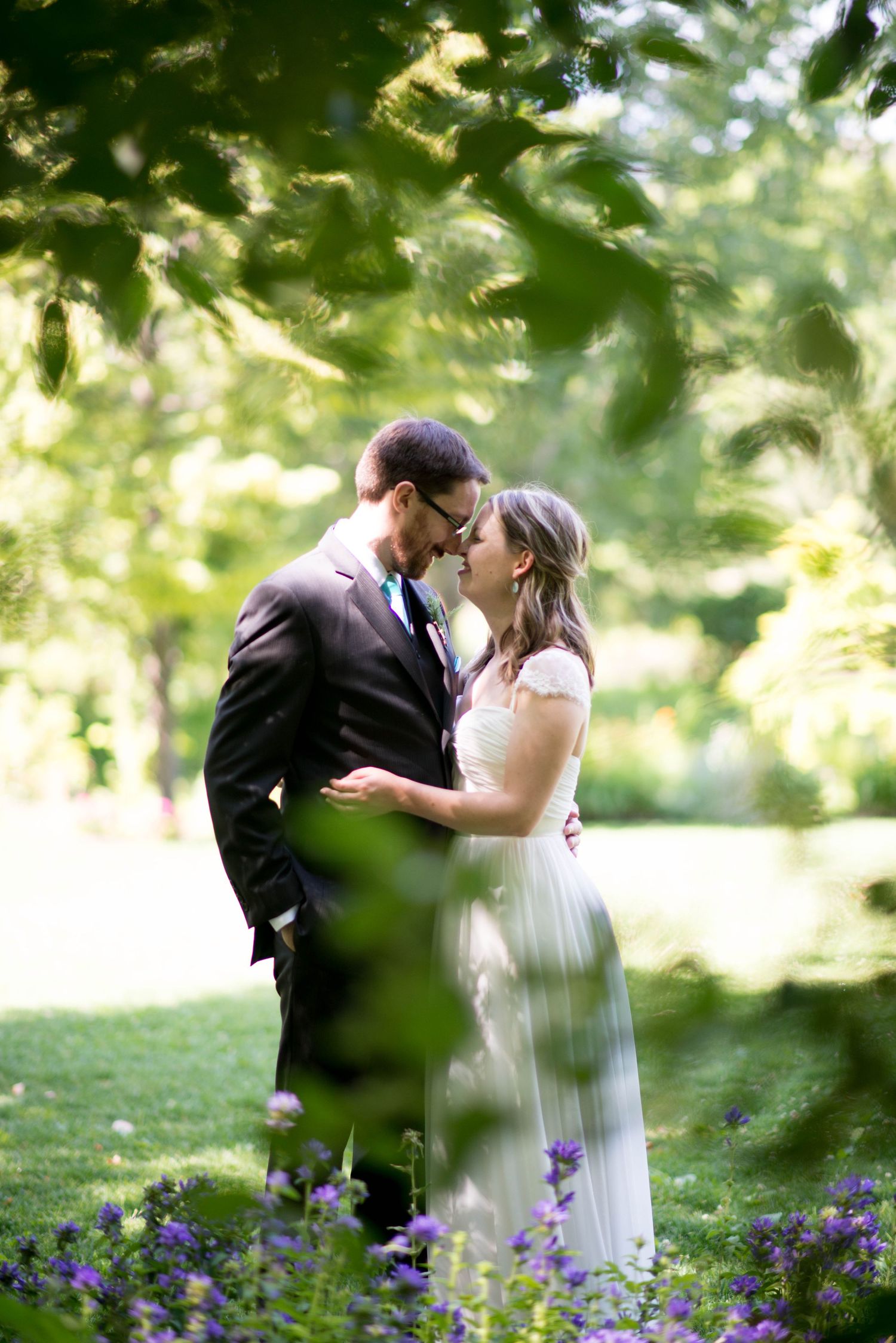 Bride and groom nearly kissing in a lush garden framed by green leaves.