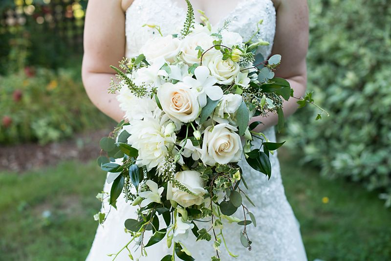Bride holding a cascading bridal bouquet of white roses and seasonal blooms before her wedding ceremony.