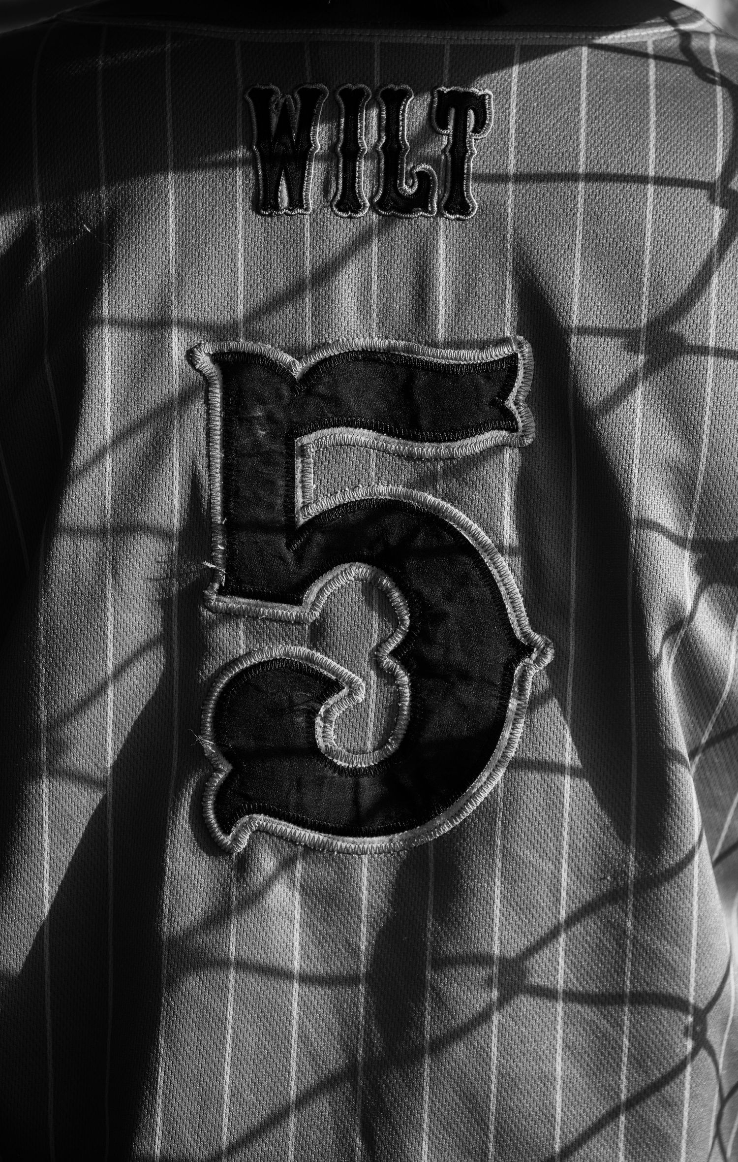 Black-and-white portrait of baseball player number 5 framed by dramatic chain-link fence shadows.