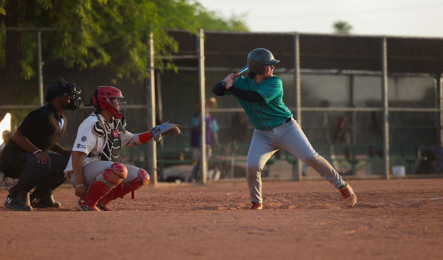 Teal-uniformed batter swings at home plate while a catcher in red gear and an umpire watch the pitch.