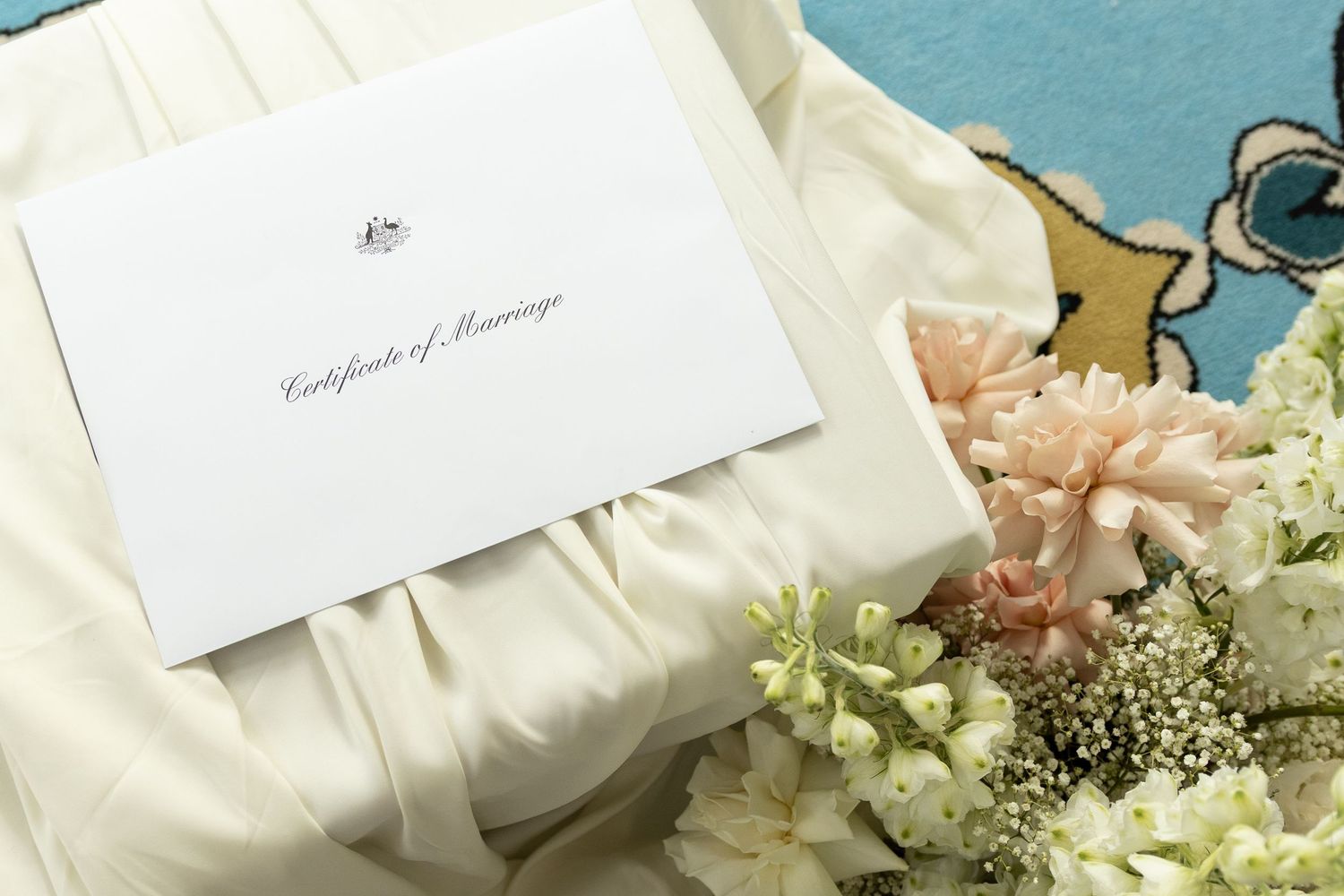 Certificate of Marriage document beside a bridal bouquet of pink and white flowers on a wedding dress.