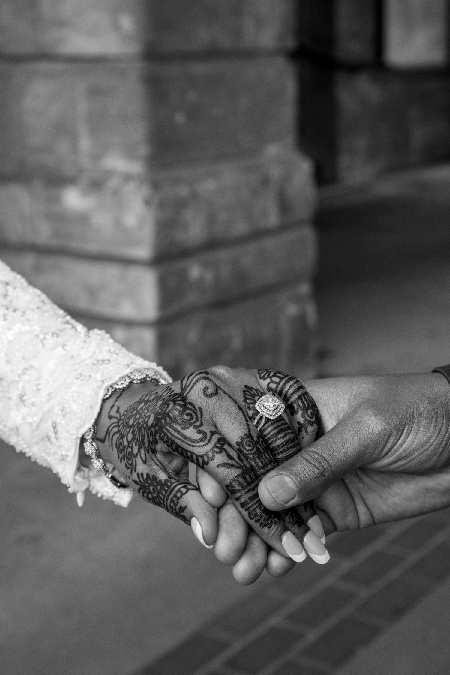 Black and white photo of a couple holding hands, bride wearing intricate henna mehndi designs and lace wedding dress.