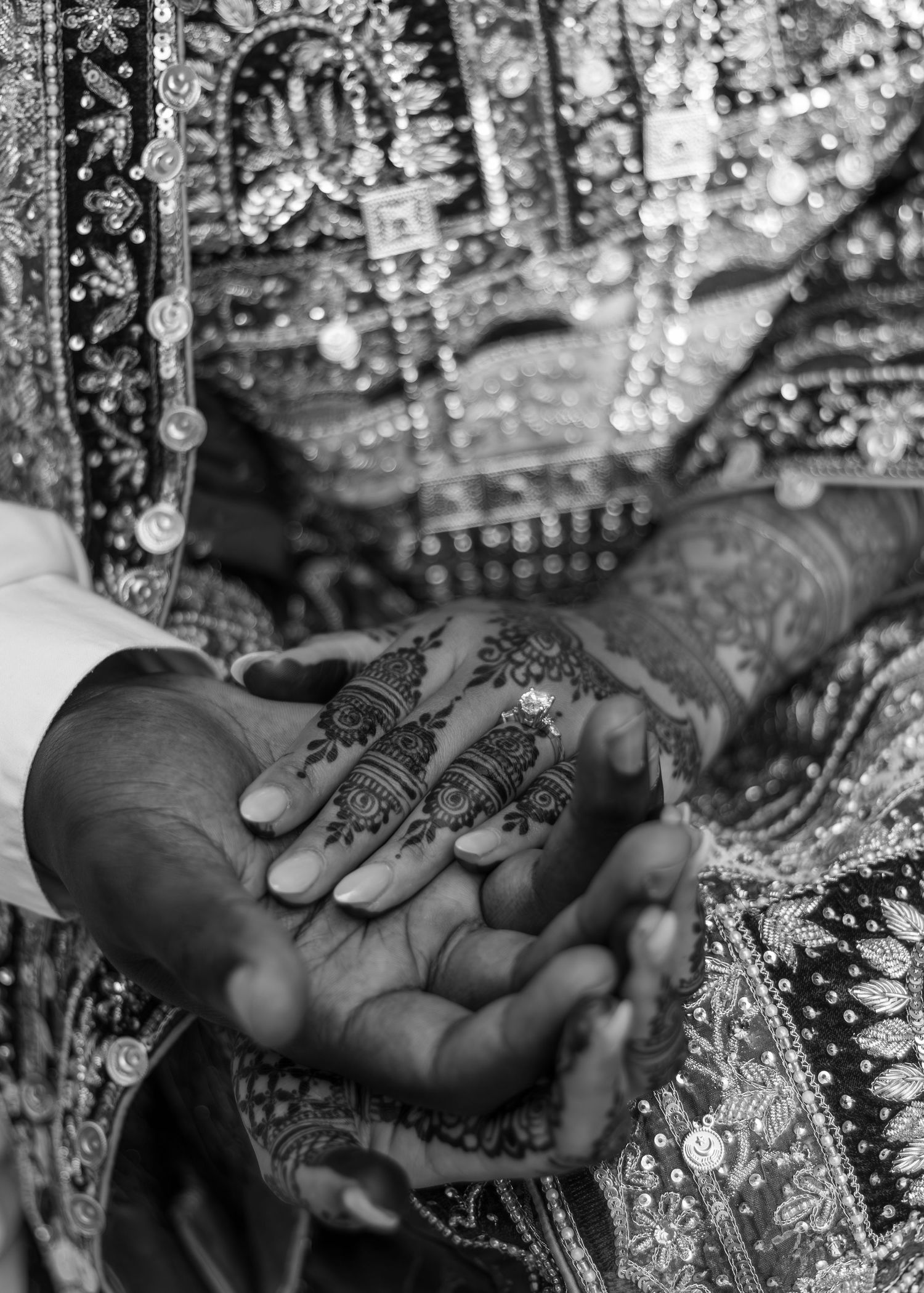 Close-up black and white photo of Indian bride's henna-adorned hands in traditional embroidered wedding attire.